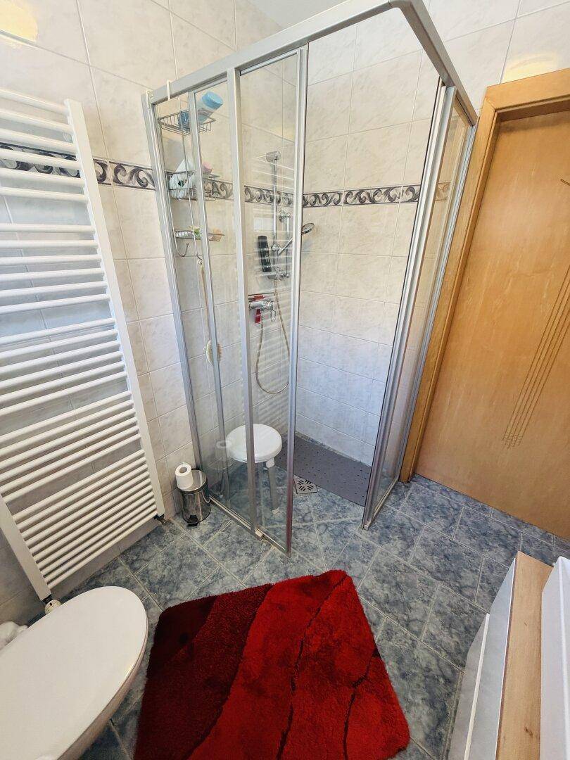 Helles Badezimmer mit Duschkabine, WC und beheiztem Handtuchhalter.