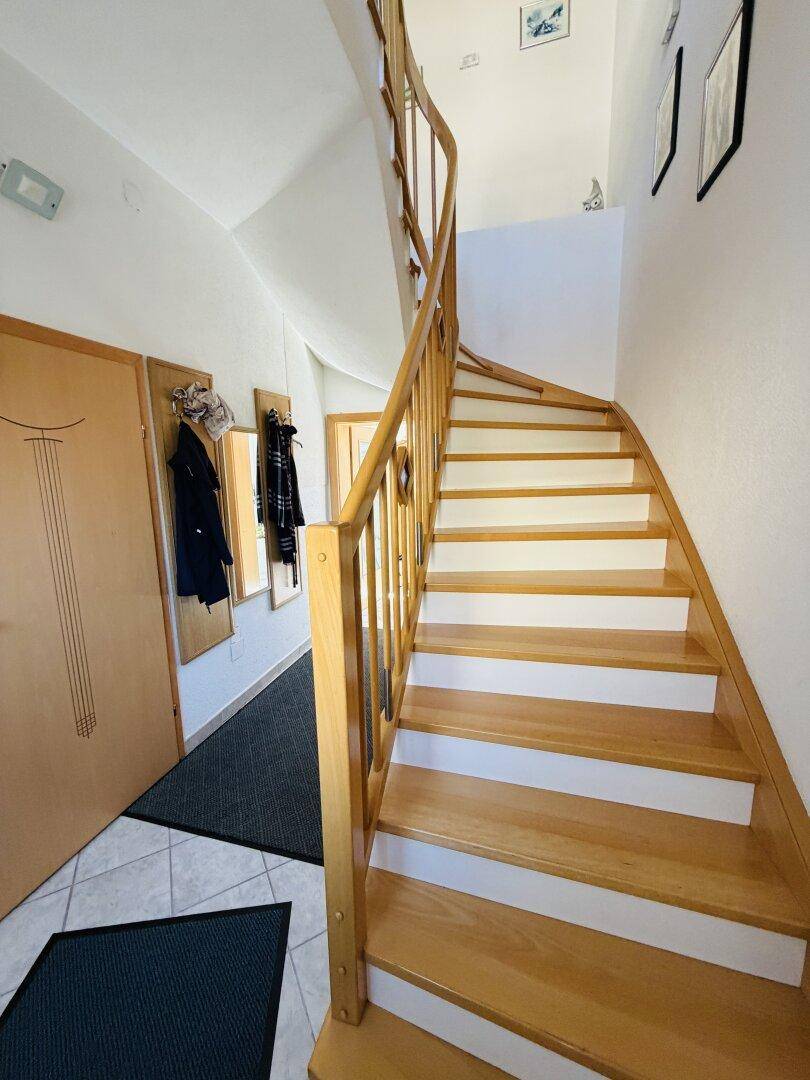 Helle Holztreppe im Eingangsbereich mit Garderobe und Fliesenboden.