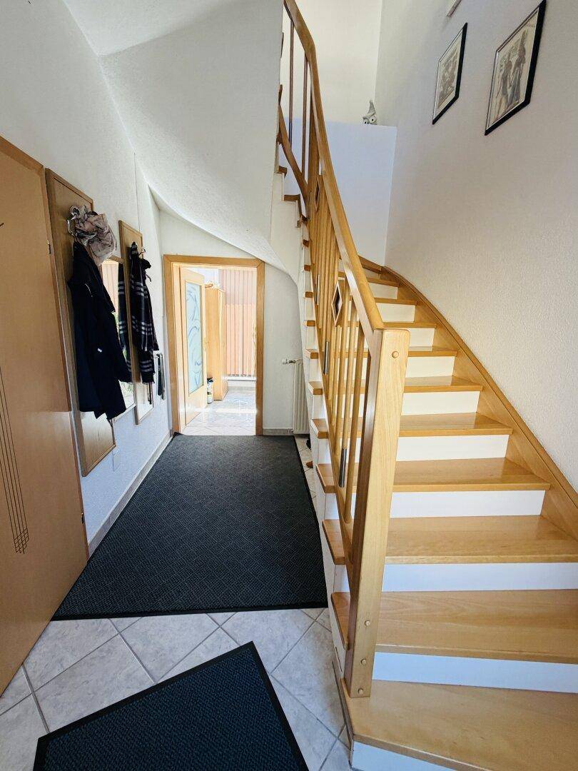Heller Eingangsbereich mit Holztreppe, Garderobe und Fliesenboden.