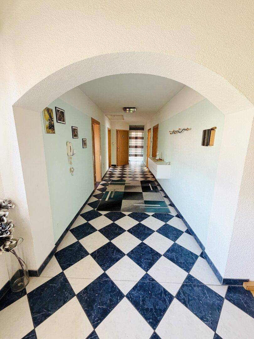 Langer Flur mit Schachbrettmuster-Fliesenboden und hellblauen Wänden.
