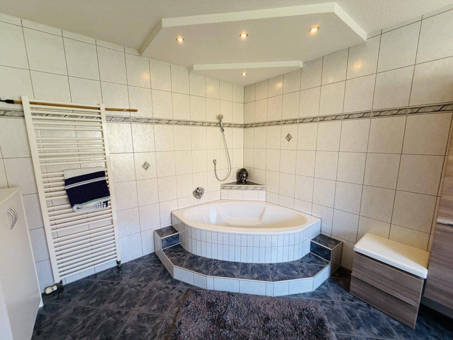 Modernes Badezimmer mit Eckbadewanne, Duschvorrichtung und Handtuchheizkörper an der Wand.