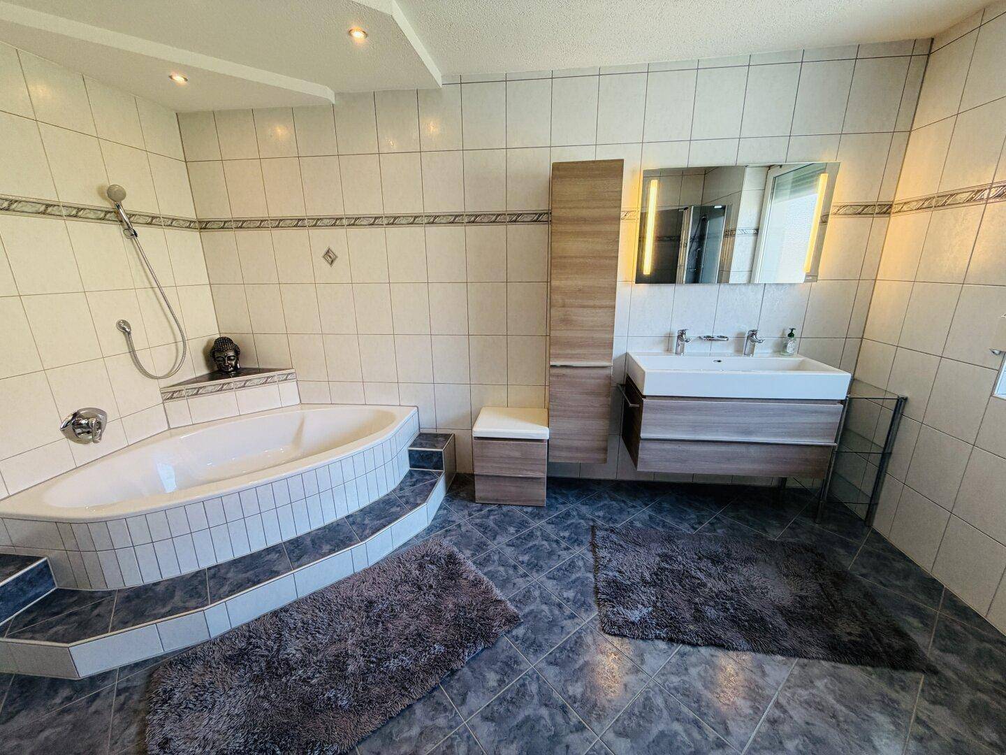 Helles Badezimmer mit Doppelwaschbecken, Eckbadewanne und großem Spiegelschrank über dem Waschtisch.