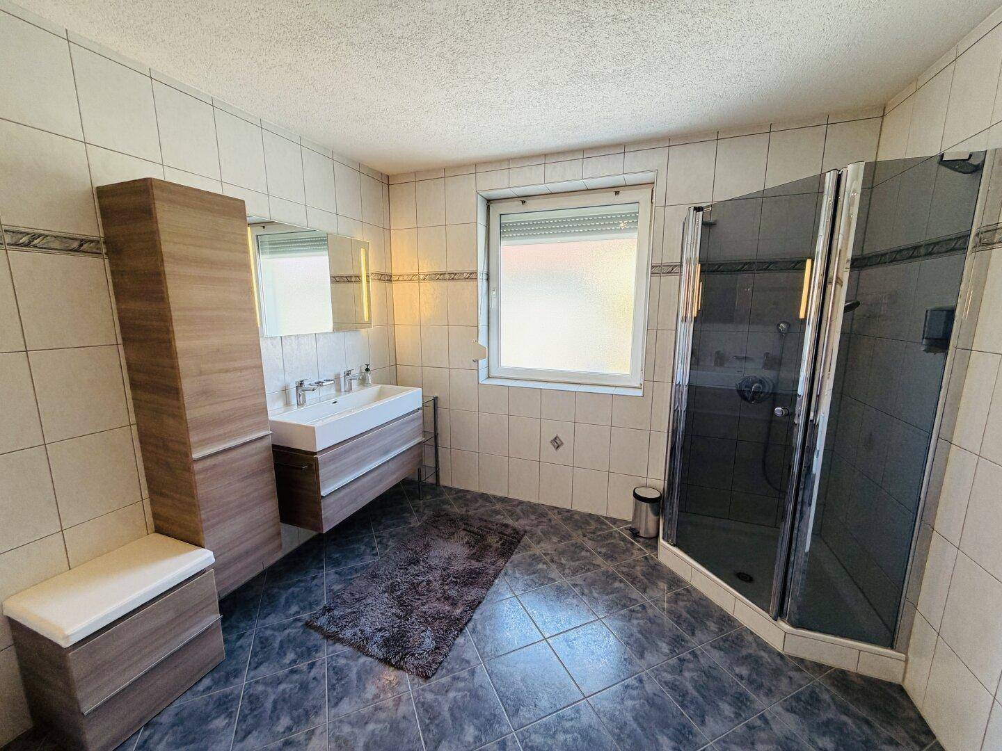 Badezimmer mit Duschkabine, Einzelwaschbecken und Fenster für natürliches Licht und Belüftung.