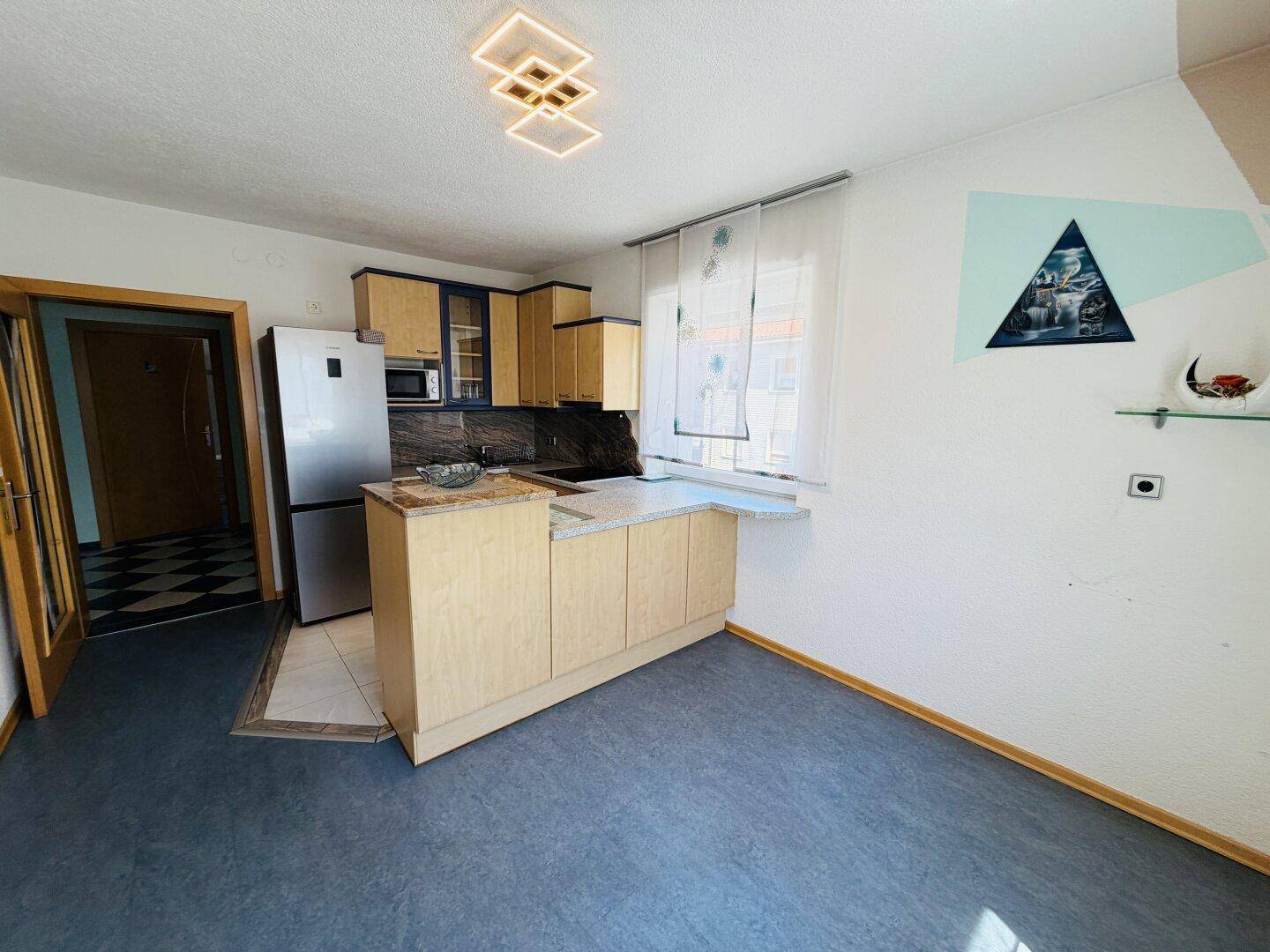 Funktionale Küche mit Kühlschrank, Mikrowelle und integrierter Arbeitsplatte mit Sitzgelegenheit.