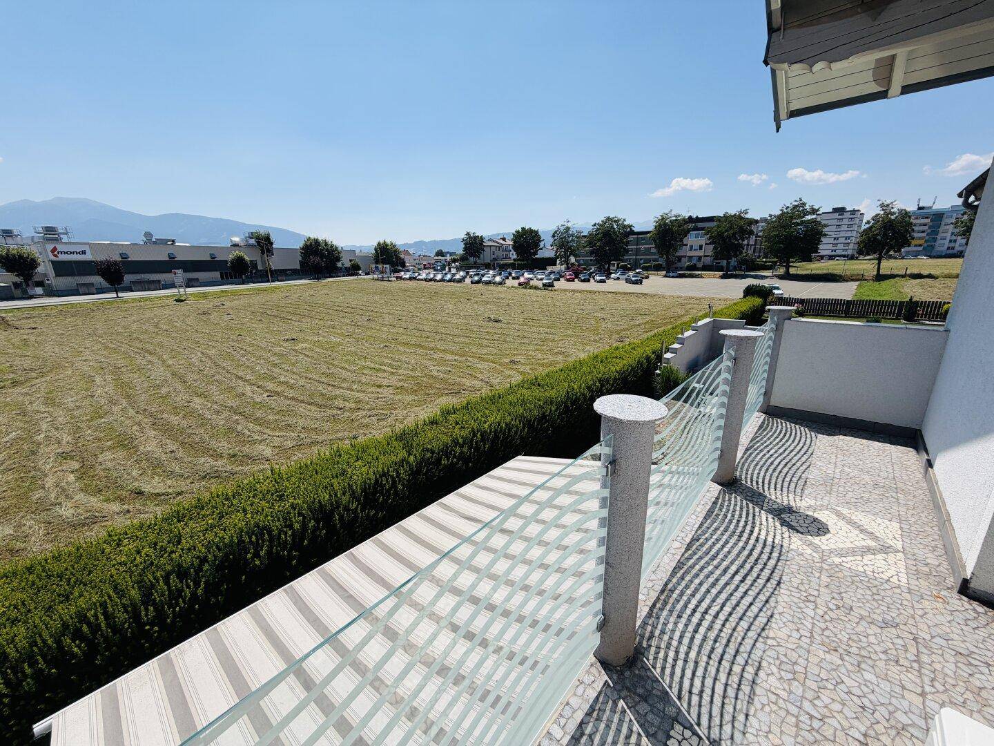 Balkon mit Glasgeländer und weitem Blick über eine Wiese und die umliegende Landschaft.