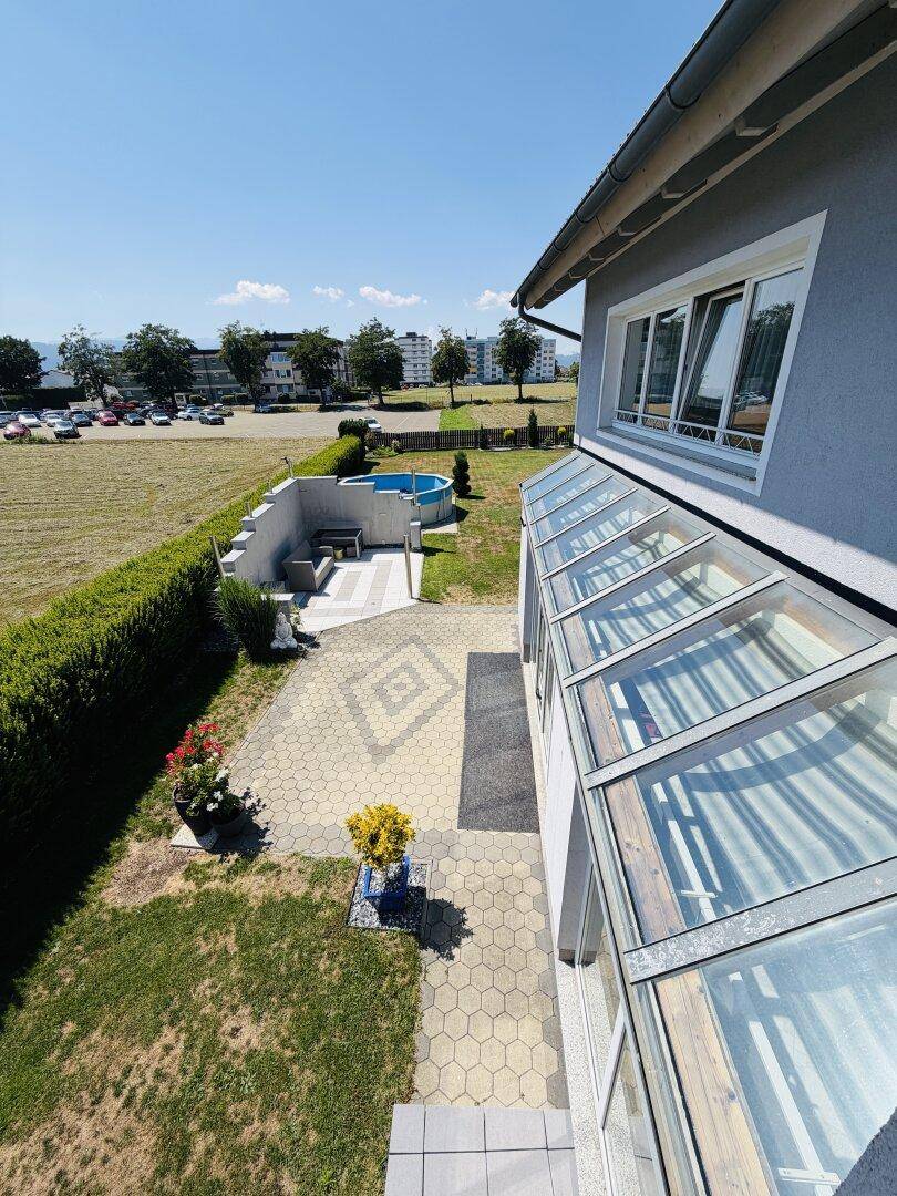Außenansicht des Hauses mit Wintergarten, gepflastertem Bereich und Garten mit Pool.