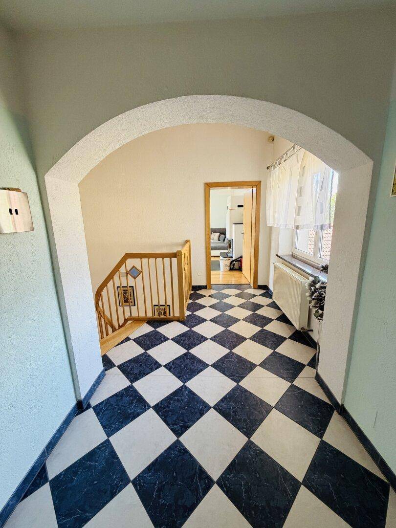 Geräumiger Flur mit Schachbrettmuster-Fliesenboden und Holztreppe zum Obergeschoss.
