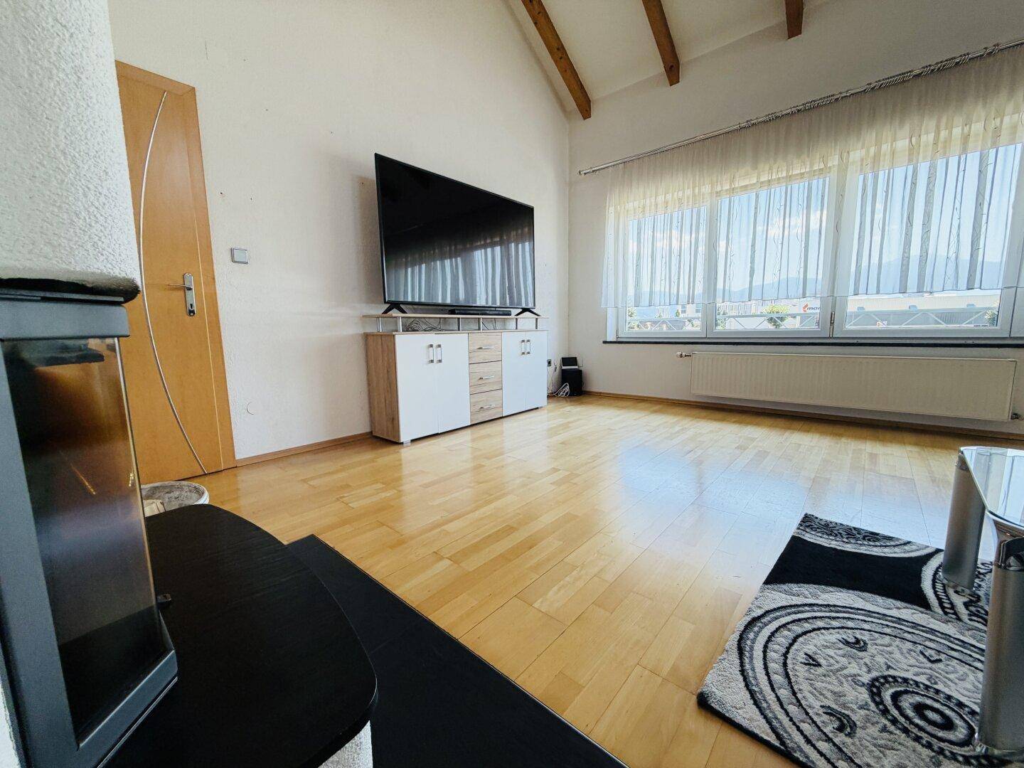 Heller Wohnbereich mit Holzboden, großem Fenster und modernem Sideboard unter dem Fernseher.