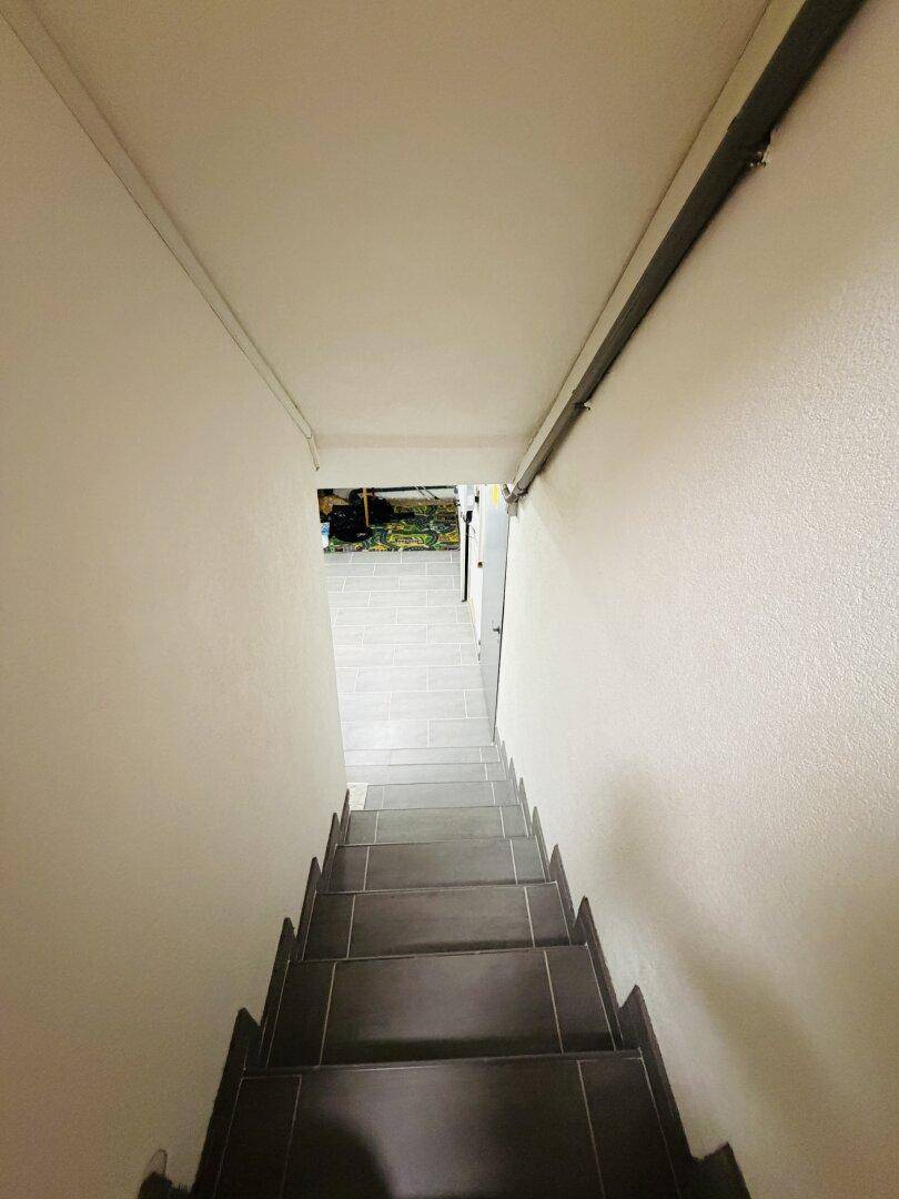 Treppenabgang in den Kellerbereich mit gefliestem Boden und schlichten, weißen Wänden.