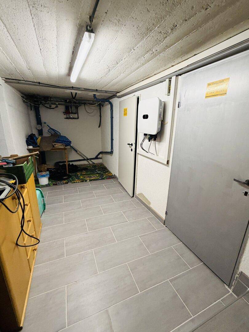 Kellerraum mit gefliestem Boden, Lagerregalen und technischer Installation an der Wand.