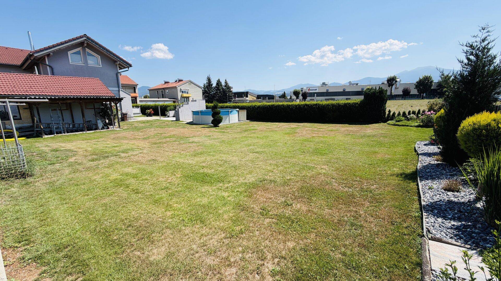 Großer Gartenbereich mit Rasenfläche, Aufstellpool und Blick auf die umliegende Landschaft.