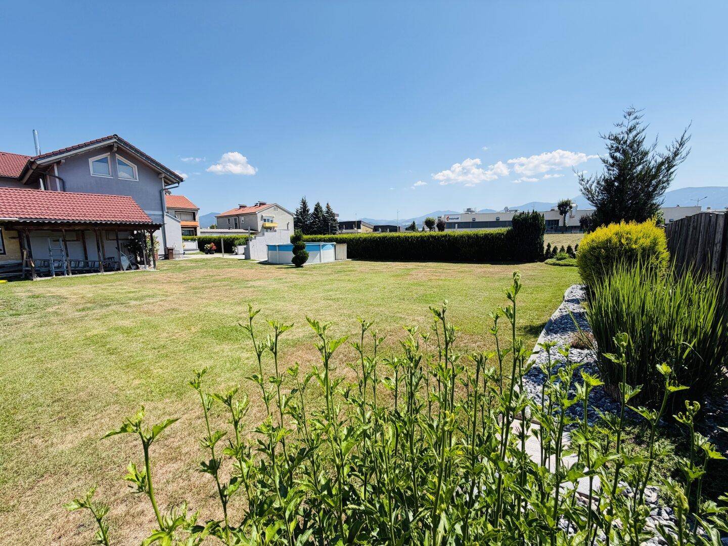 Großer, gepflegter Garten mit Rasenfläche, Hecke und kleinem Pool im Hintergrund.
