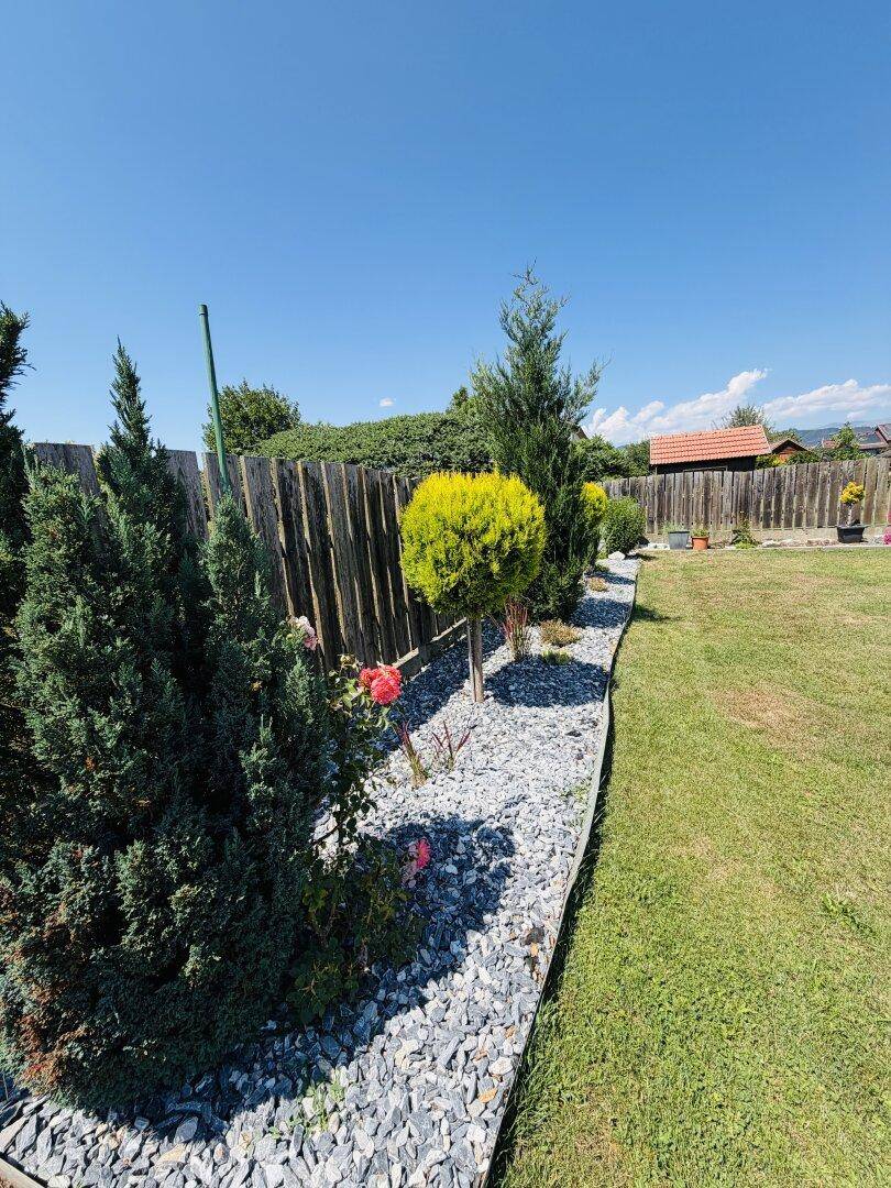 Gepflegter Gartenweg mit Zierkies, verschiedenen Pflanzen und Holzzaun im Hintergrund.