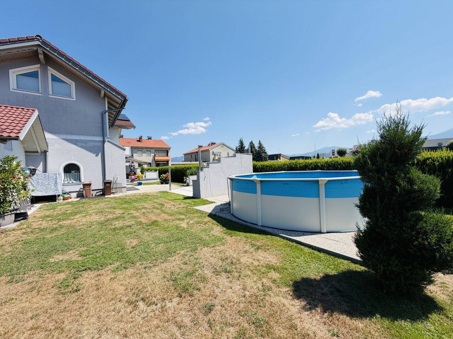 Seitenansicht des Hauses mit großem Garten, Aufstellpool und Blick auf die Nachbarschaft.