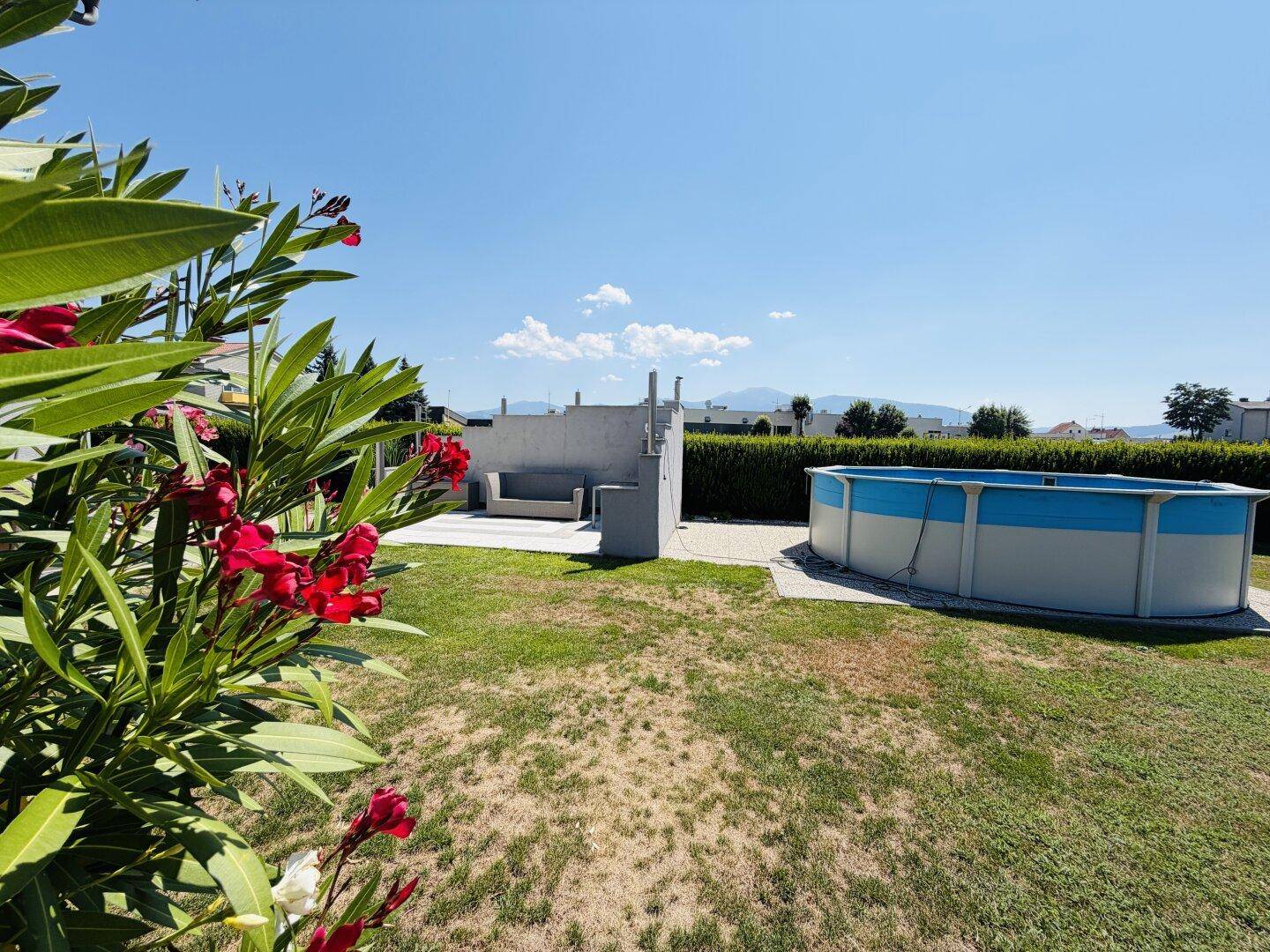Weitläufiger Garten mit blühendem Oleander, Aufstellpool und einer gemütlichen Sitzecke.