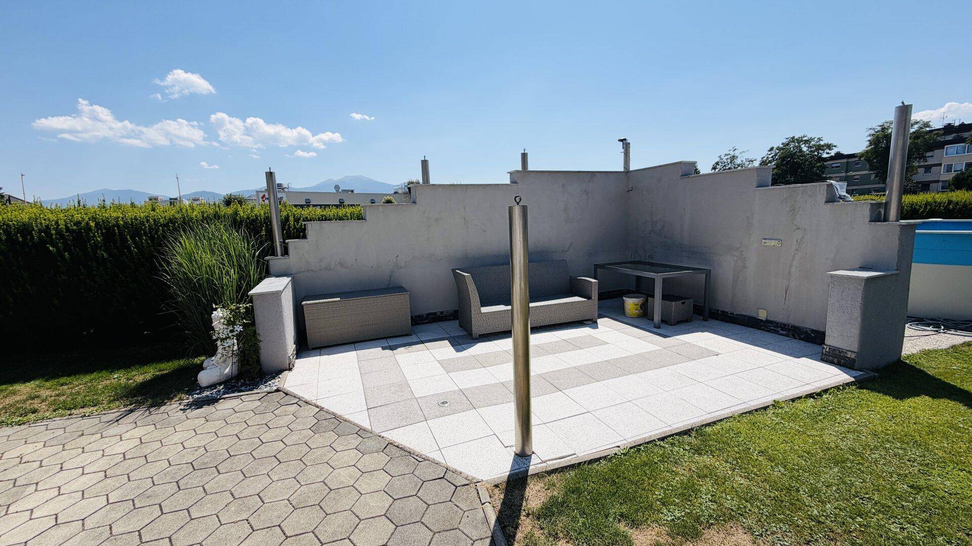 Moderne gepflasterte Terrasse mit bequemen Outdoor-Möbeln und schützenden Betonwänden.