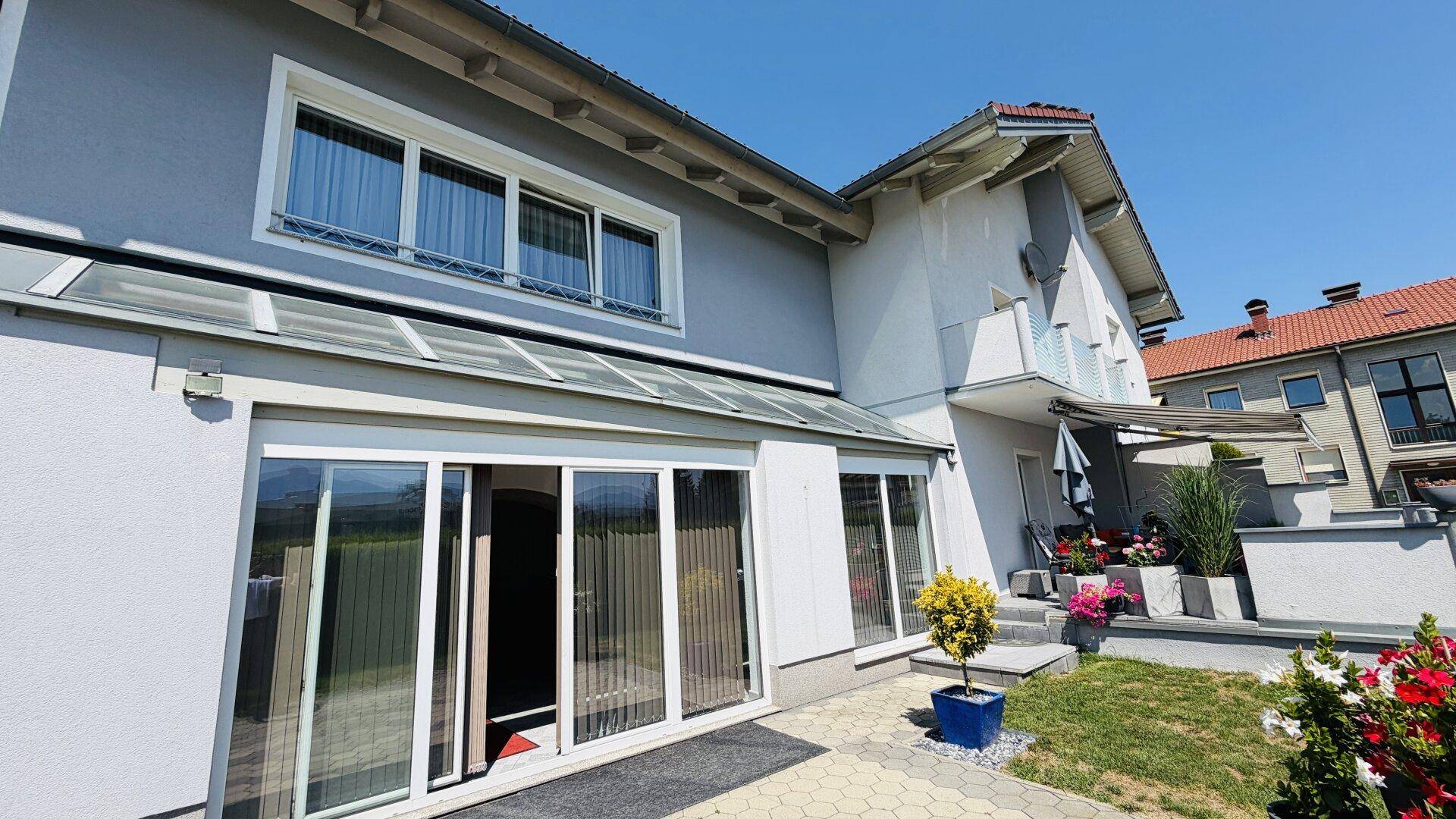 Rückseite des Hauses mit großen Glasschiebetüren, Fenstern und einer ausfahrbaren Markise.