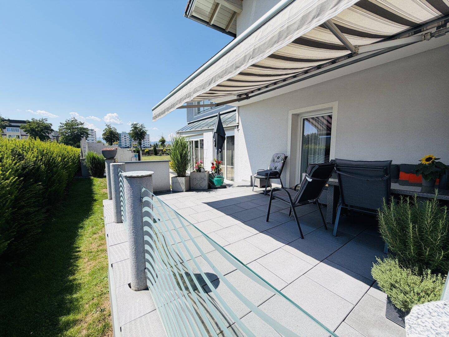 Geräumige Terrasse mit modernen Gartenmöbeln, Glasgeländer und ausziehbarer Markise.
