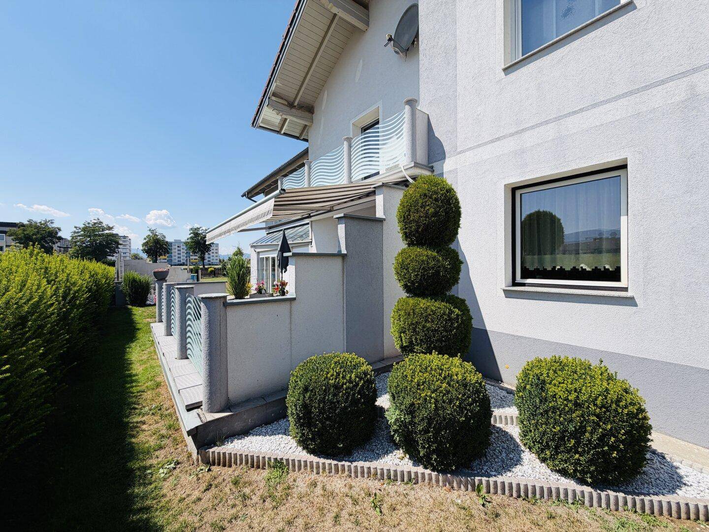 Seitenansicht des Hauses mit dekorativen Buchsbaumkugeln, Kiesbeet und kleinem Balkon.