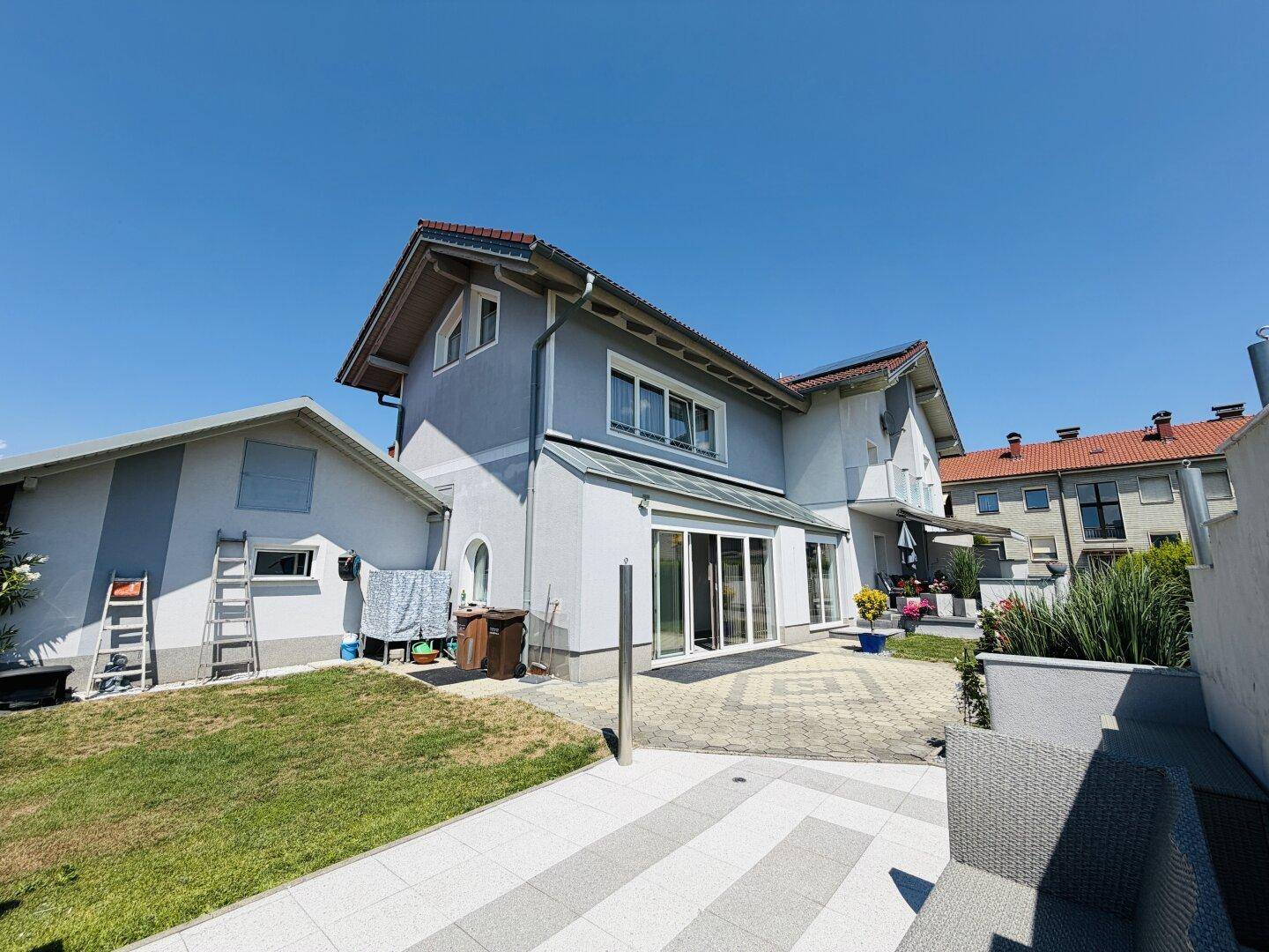 Rückansicht des Hauses mit Anbau, gepflastertem Bereich und weitläufigem Garten.