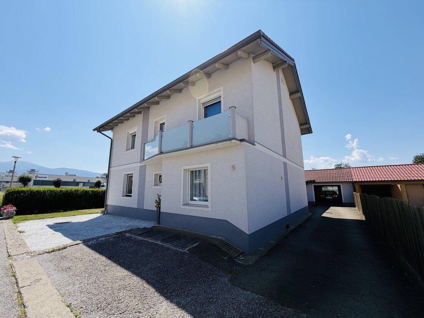 Vorderansicht des Hauses mit kleinem Balkon, Kiesfläche und Zufahrt zur Garage.