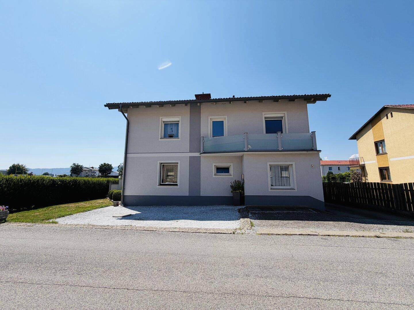 Frontansicht des modernen Hauses mit Balkon, gepflegter Kiesfläche und ruhiger Straße.