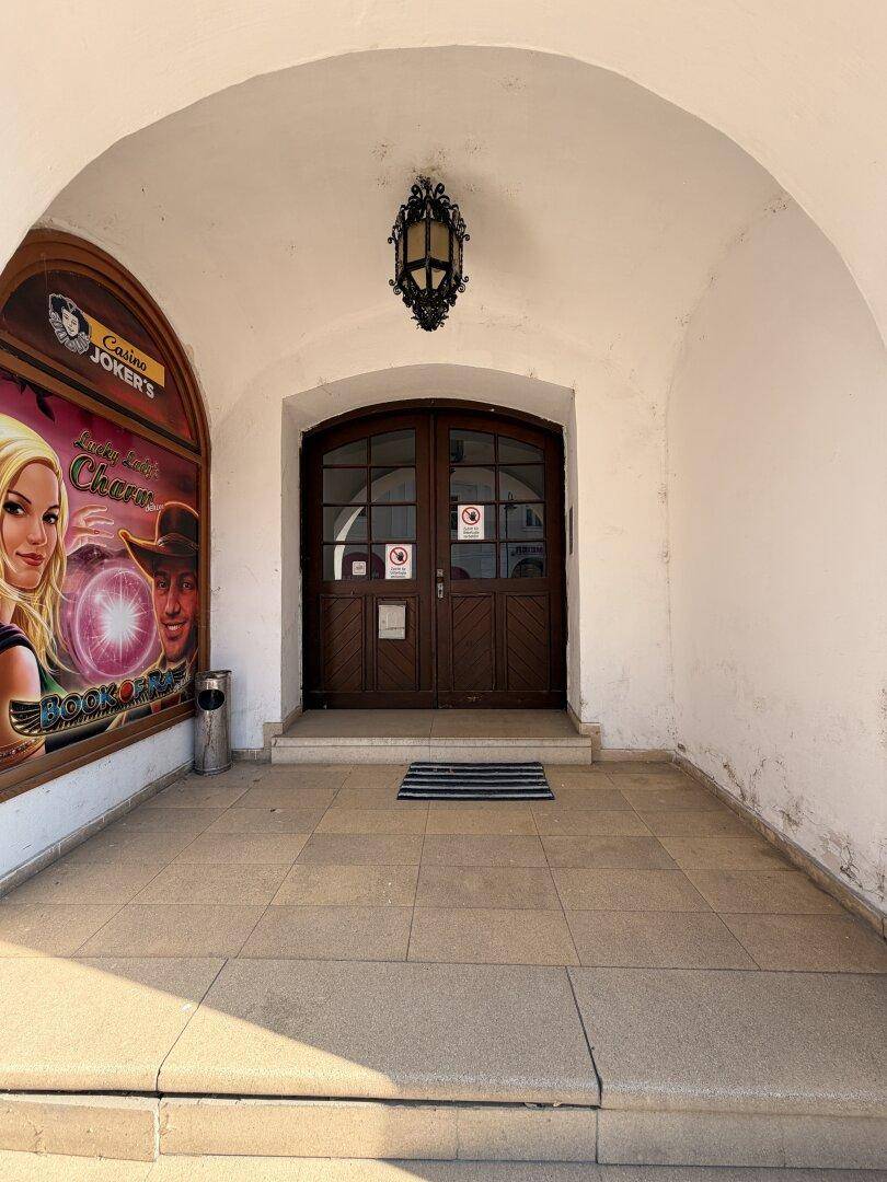Eingangsbereich unter einem Bogen mit einer doppelten Holztür und einer Werbetafel.