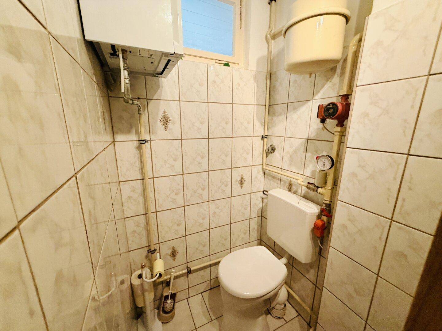 Kleines WC mit Fliesen an den Wänden und einem Fenster für natürliche Belüftung.