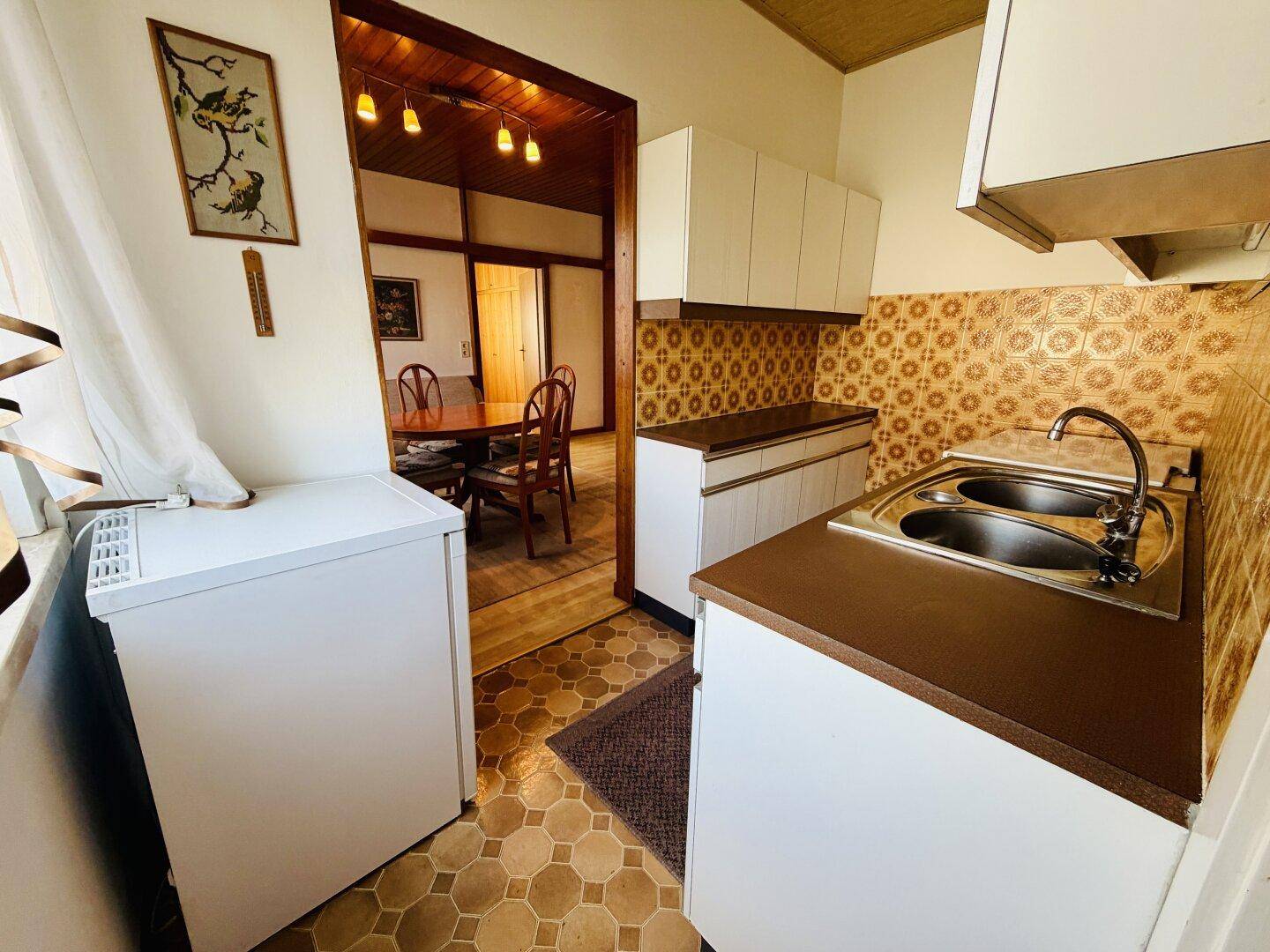 Küche mit Blick in den Wohnbereich, ausgestattet mit Spüle und Kühlschrank.