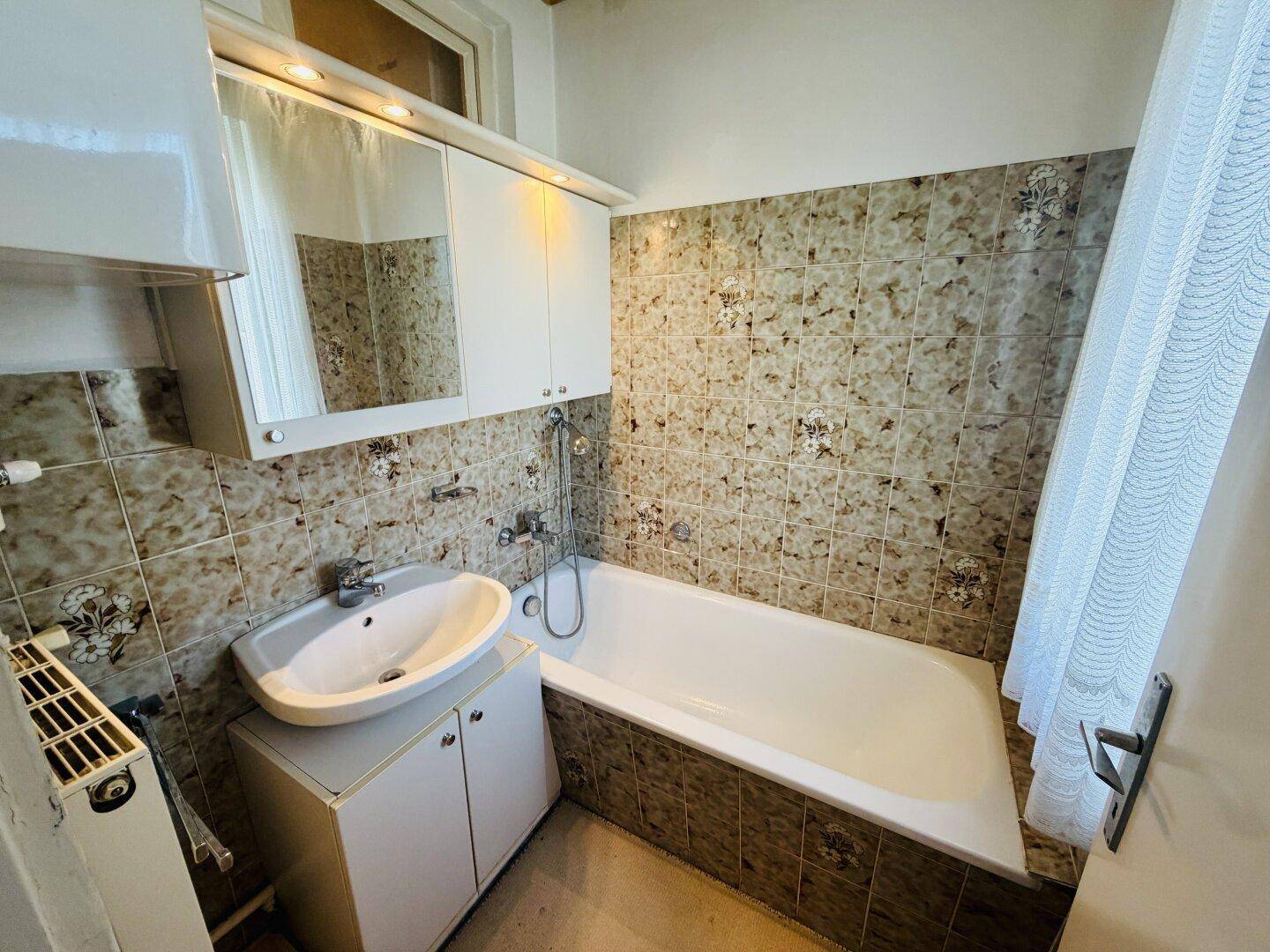 Badezimmer mit Badewanne, Waschbecken und Spiegelschrank, gefliest in traditionellem Stil.