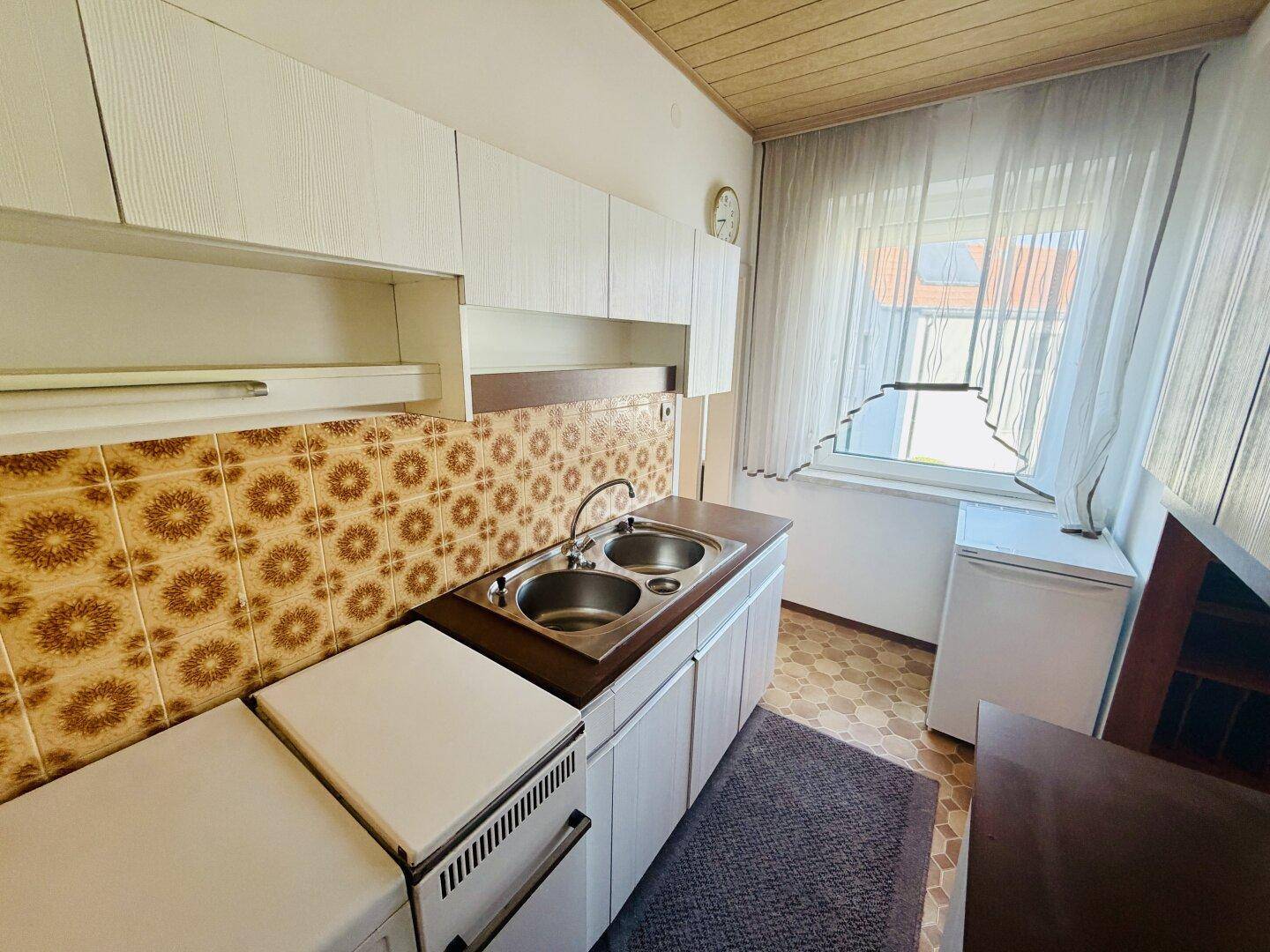 Helle Küche mit Fenster, Doppelspüle und traditionellen Fliesen, inklusive Kühlschrank.