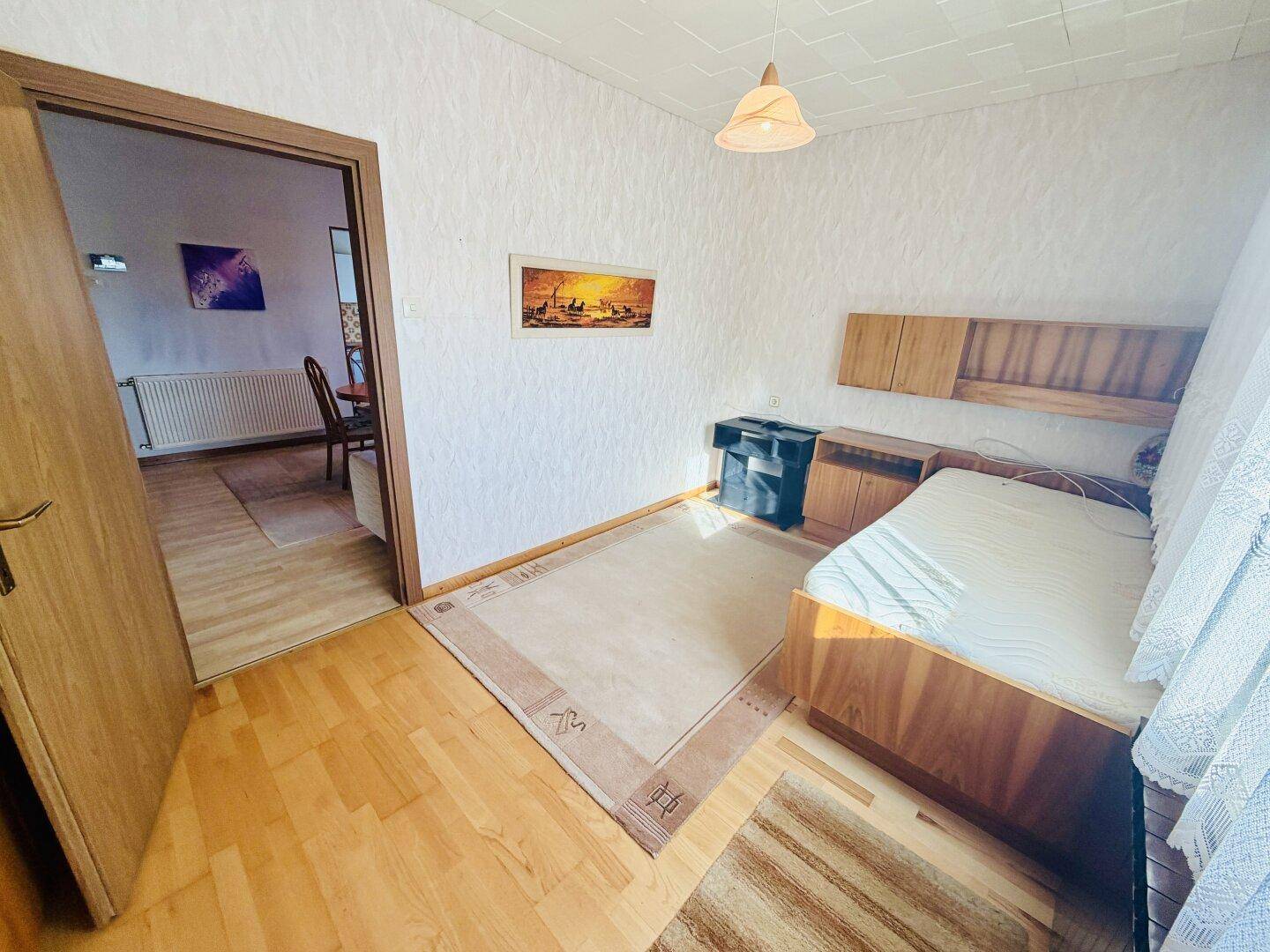 Schlafzimmer mit Parkettboden und Zugang zum Wohnbereich, hell und funktional eingerichtet.