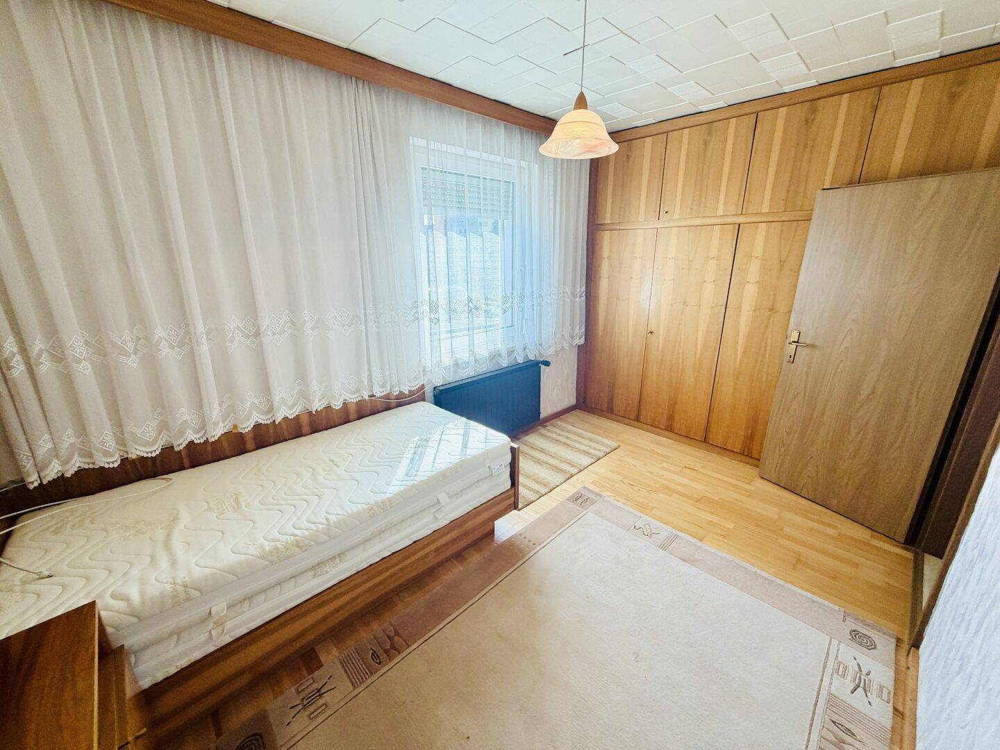 Schlafzimmer mit Holzwand, Einzelbett und großem Fenster, bietet viel Stauraum.