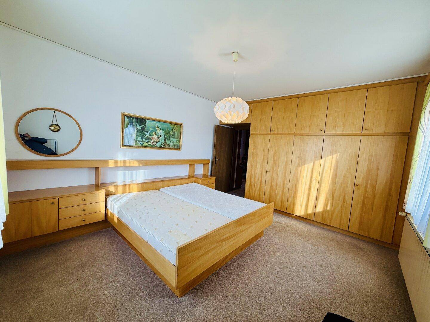 Schlafzimmer mit Doppelbett, Teppichboden und großen Holzschränken, sonnig beleuchtet.