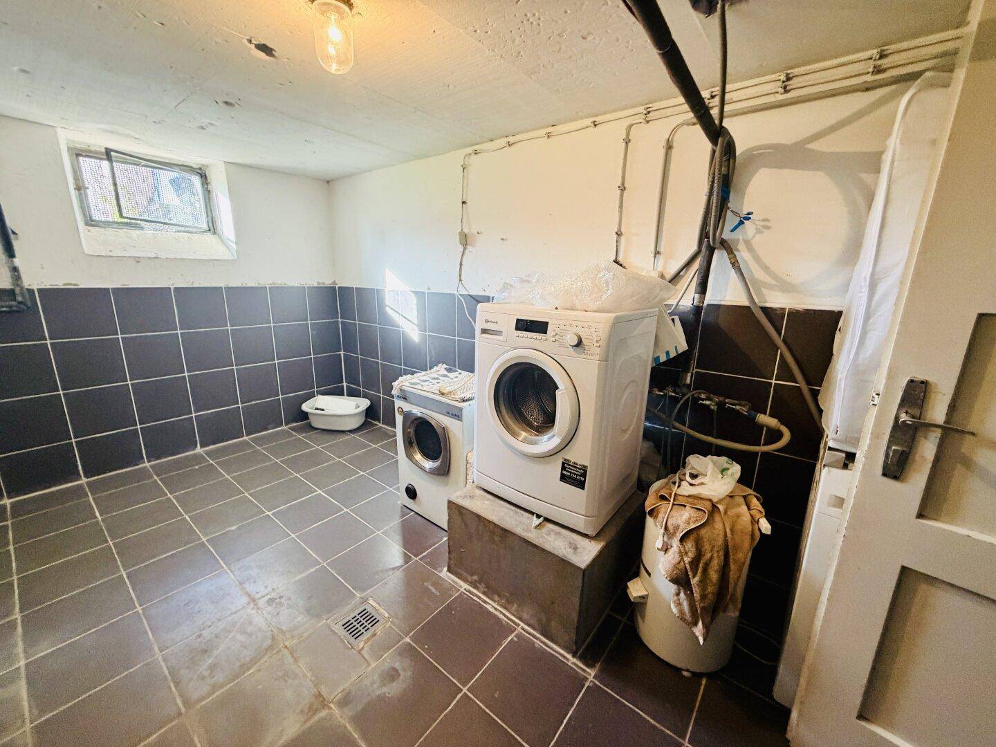 Waschküche im Keller mit Waschmaschine, Trockner und gefliestem Boden.