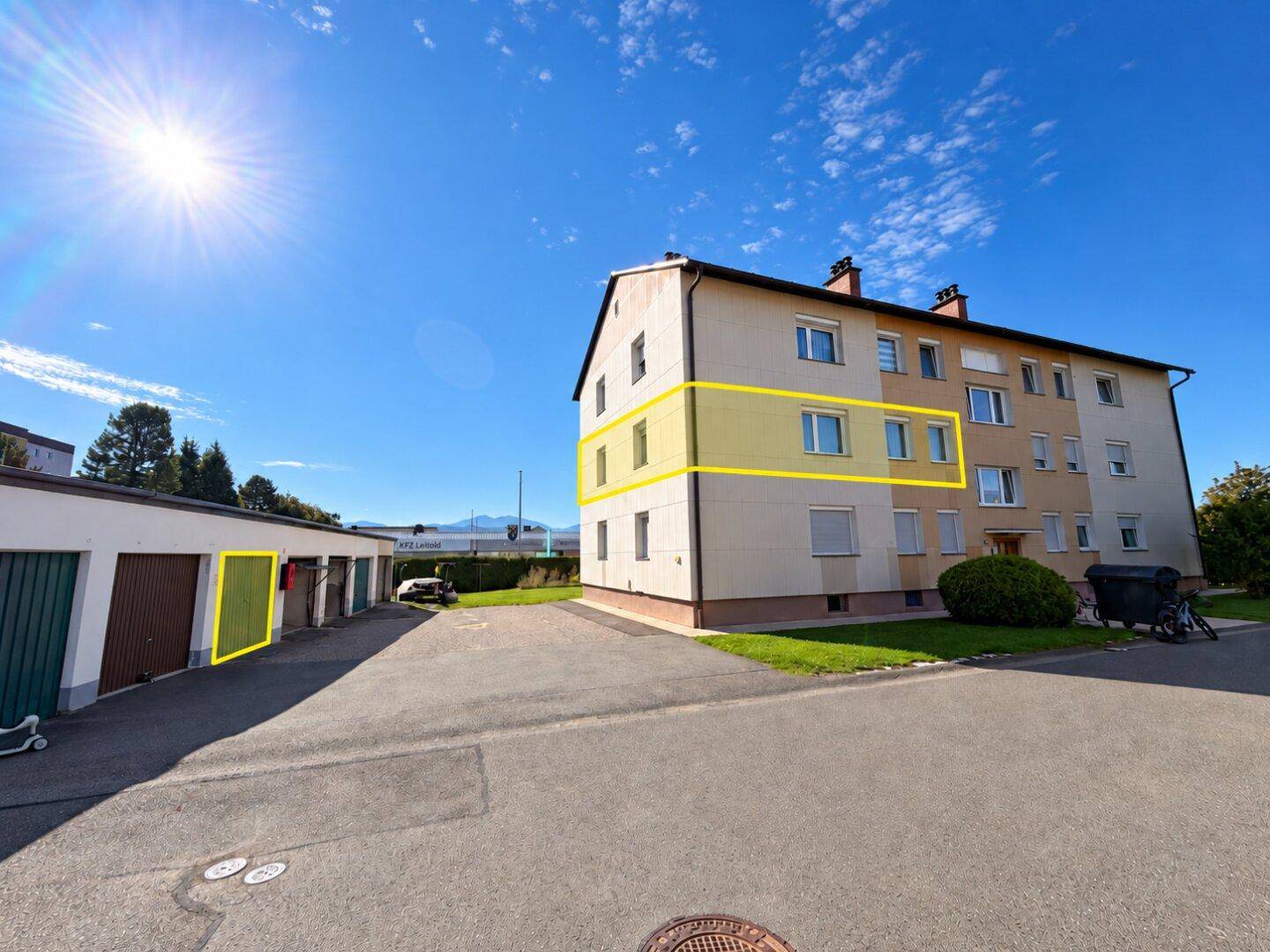 Mehrfamilienhaus mit hervorgehobener Wohnung und Garagen unter blauem Himmel.