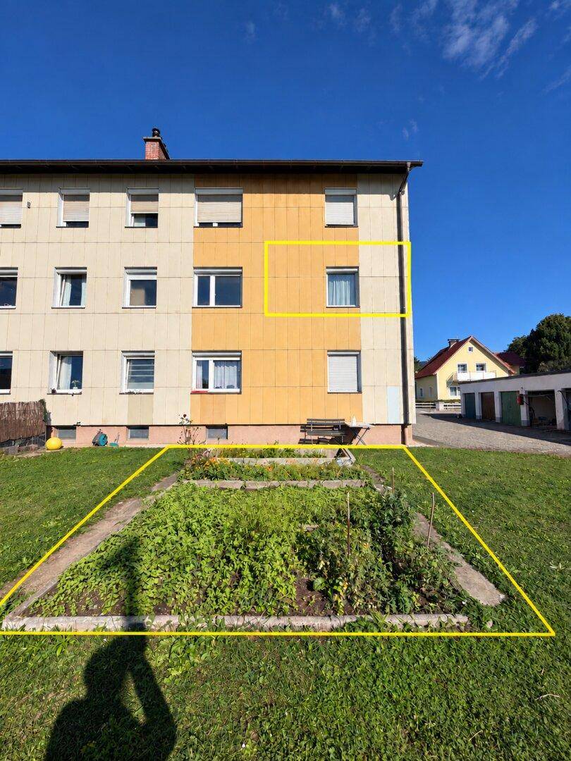 Mehrfamilienhaus mit zugehörigem Gartenbeet und Rasenfläche im Freien.