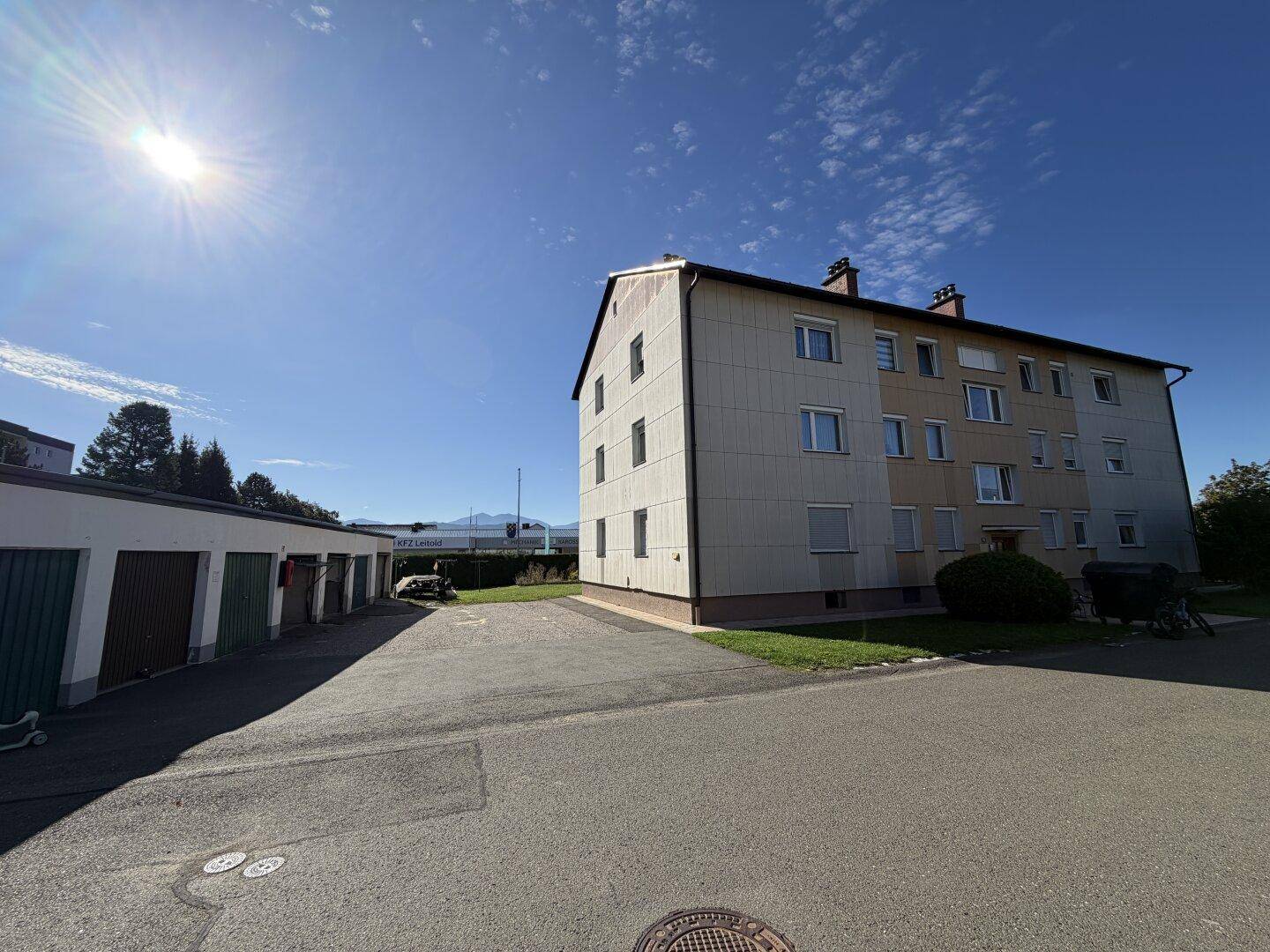 Mehrfamilienhaus mit Garagenreihe unter blauem Himmel und Sonnenschein.