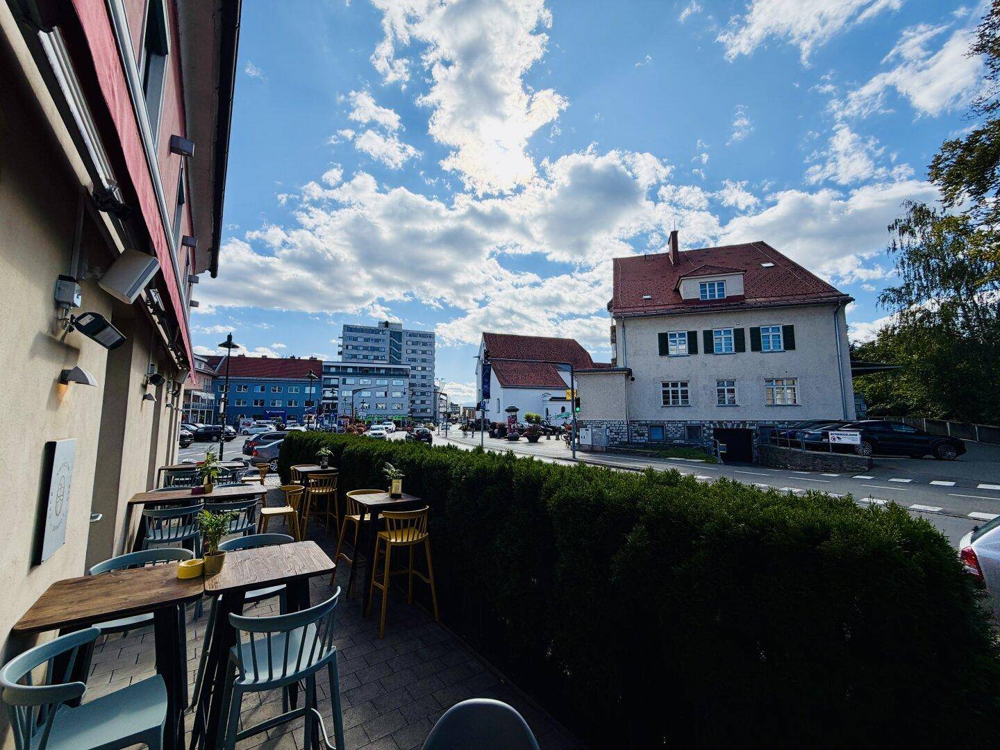Eine Außenterrasse mit Blick auf die Stadt und umliegende Gebäude, umgeben von einer grünen Hecke.
