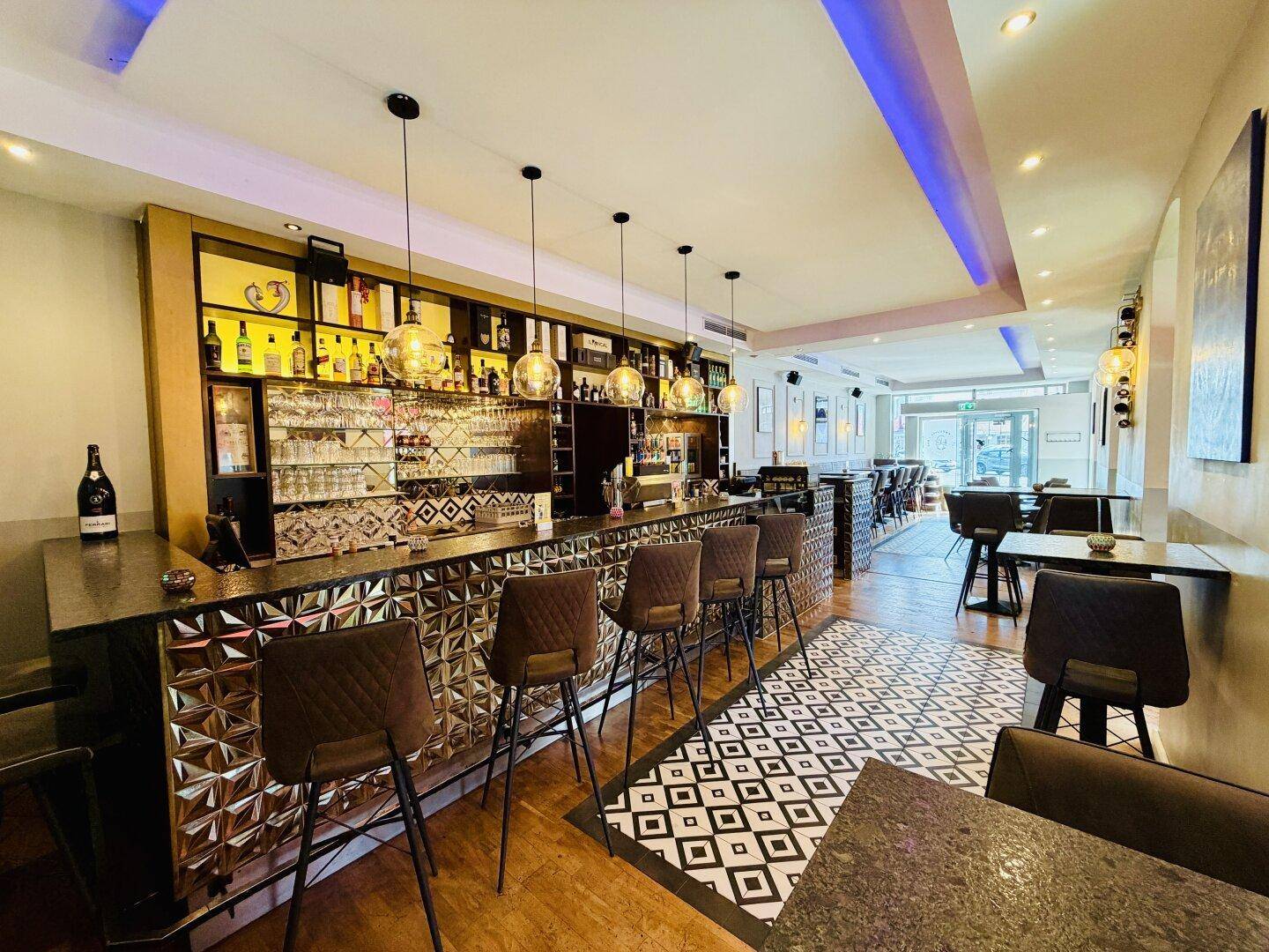 Eine moderne Bar mit dunkler Theke, bequemen Barhockern und einem auffälligen gemusterten Boden.
