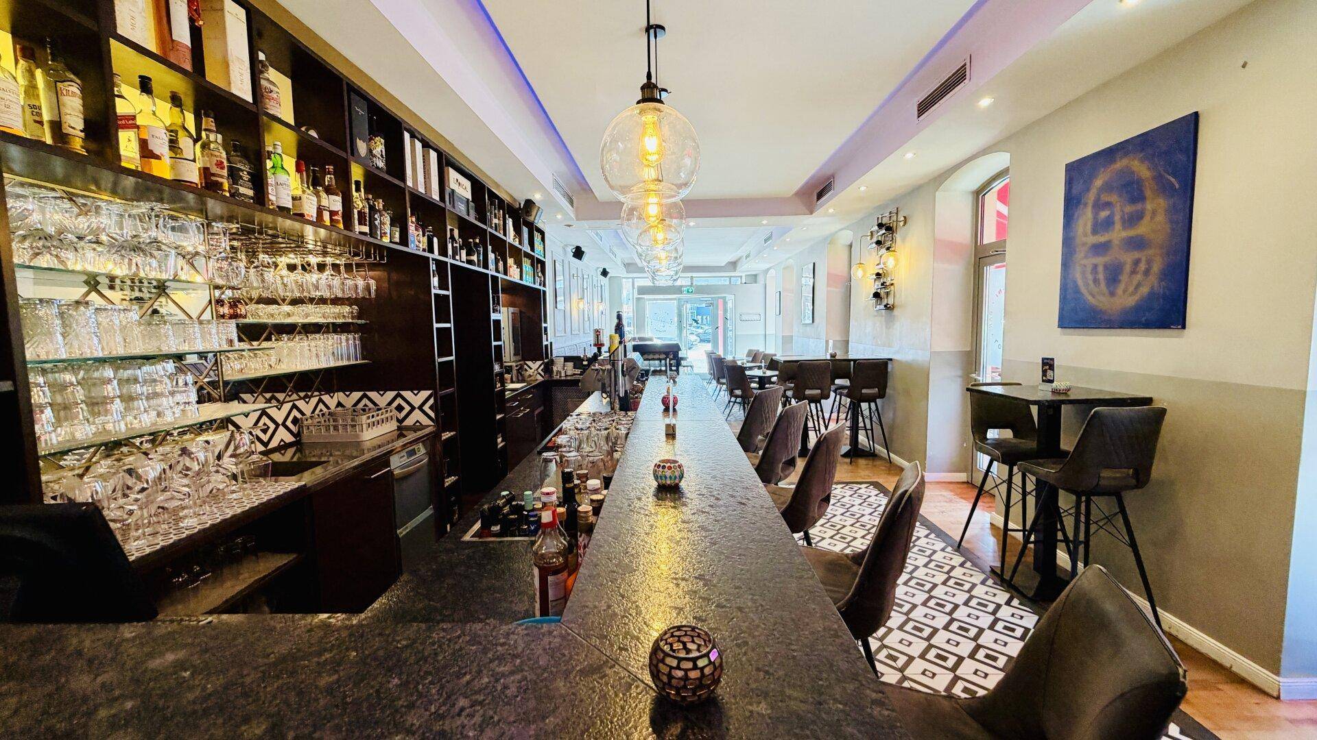 Eine lange, elegante Bar mit glänzender Oberfläche, vielen Gläsern und Flaschen sowie stilvollen Hockern.