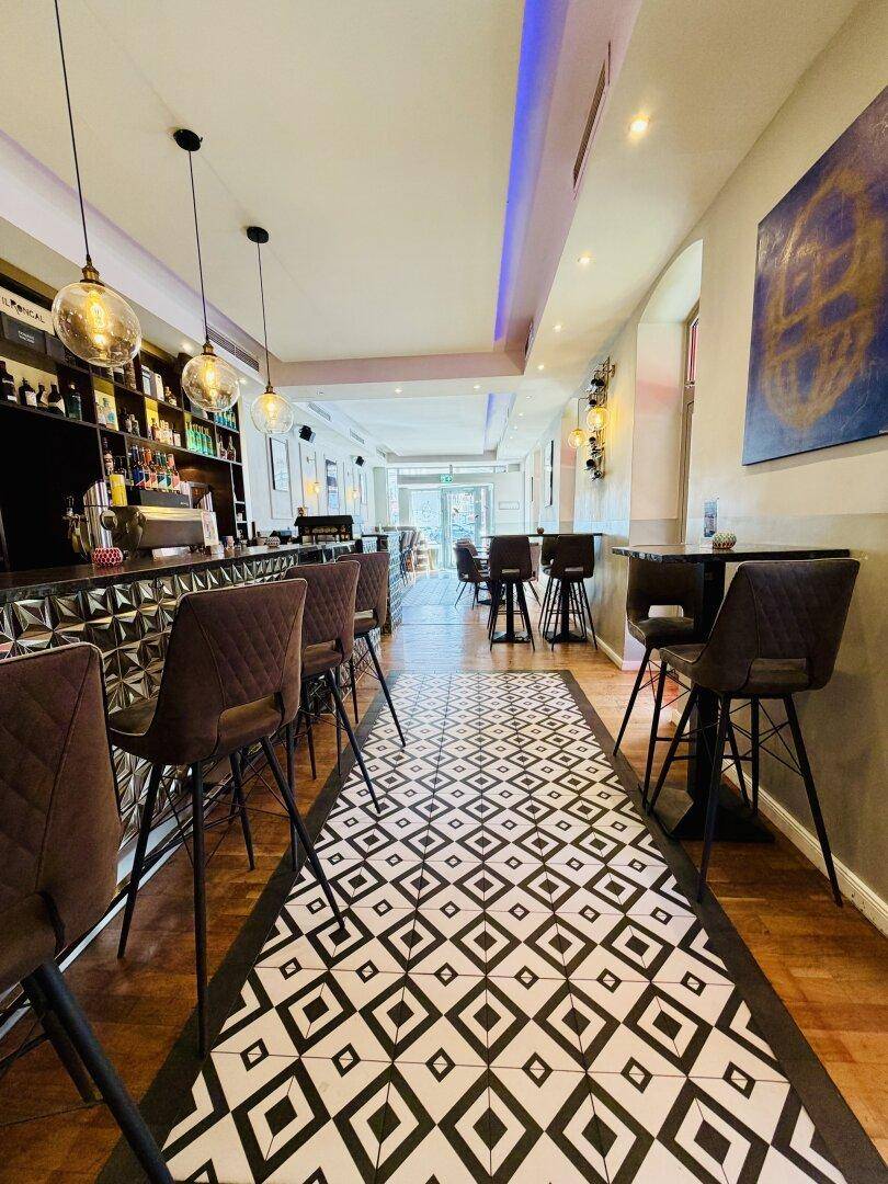 Eine lange Bar mit stilvollen Hockern und einem geometrischen Bodenmuster, das den Raum optisch verlängert.