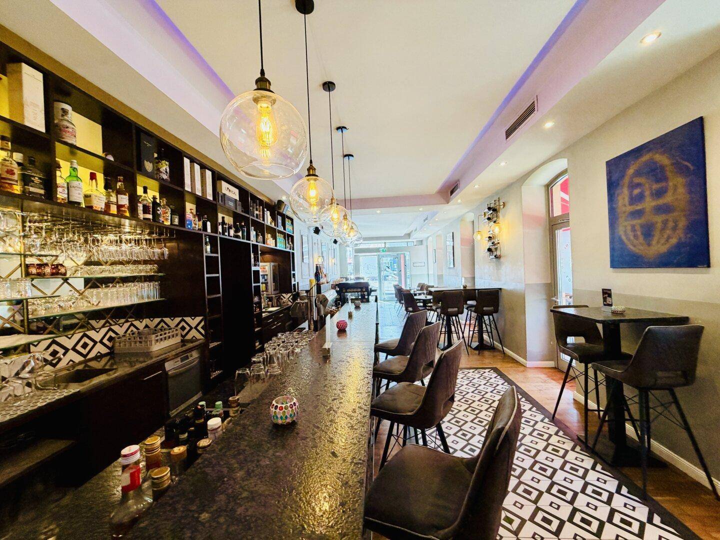 Eine moderne Bar mit dunkler Theke, dekorativen Hängelampen und einem auffälligen gemusterten Boden.
