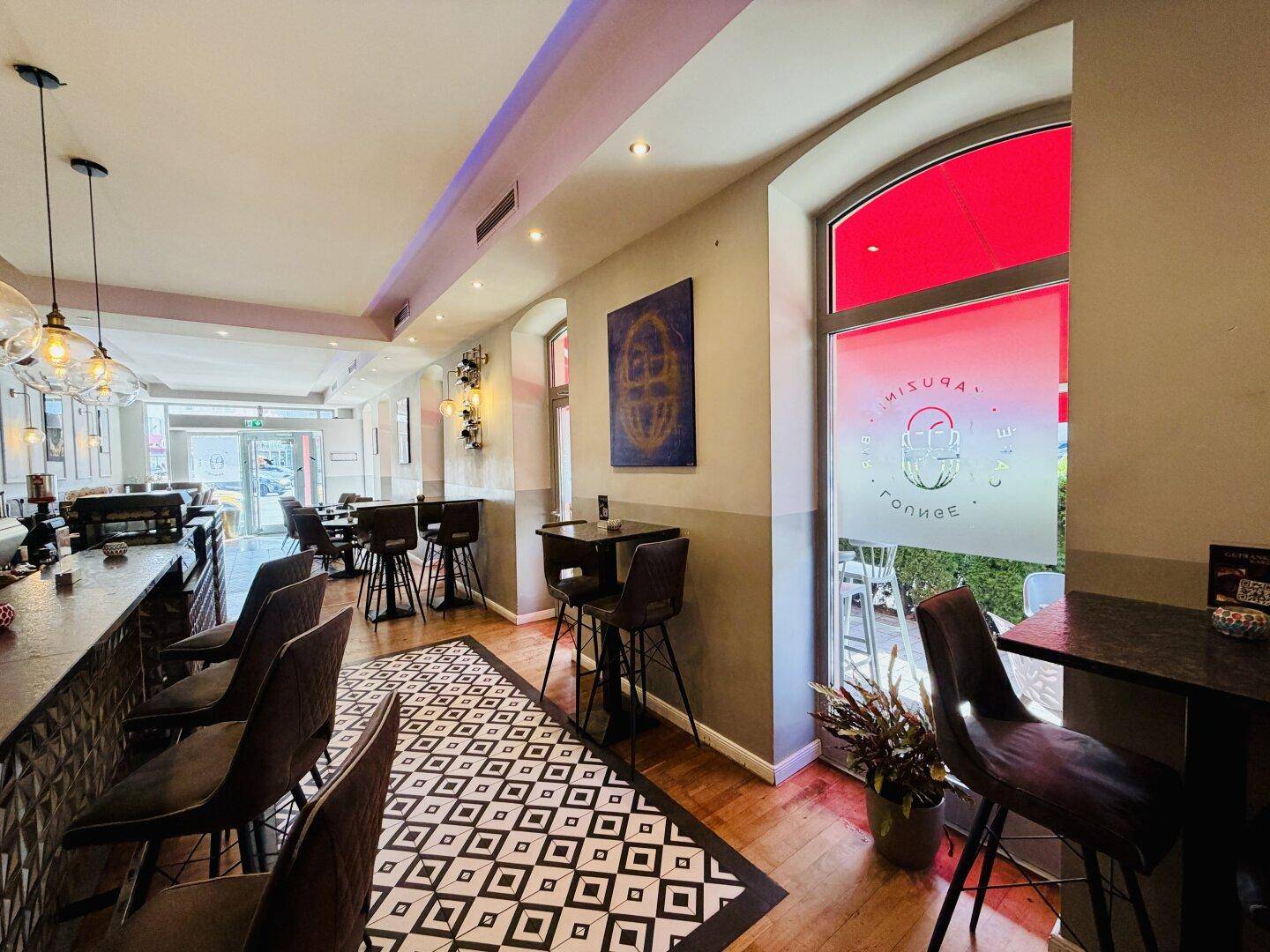 Eine moderne Bar mit dunkler Theke, dekorativen Hängelampen und einem auffälligen gemusterten Boden.