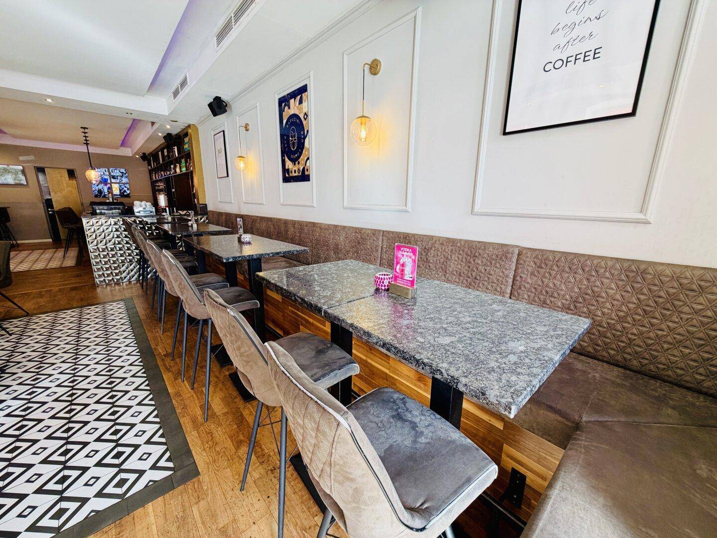 Gemütlicher Sitzbereich in einem Café mit gepolsterten Bänken, Granittischen und Holzboden.