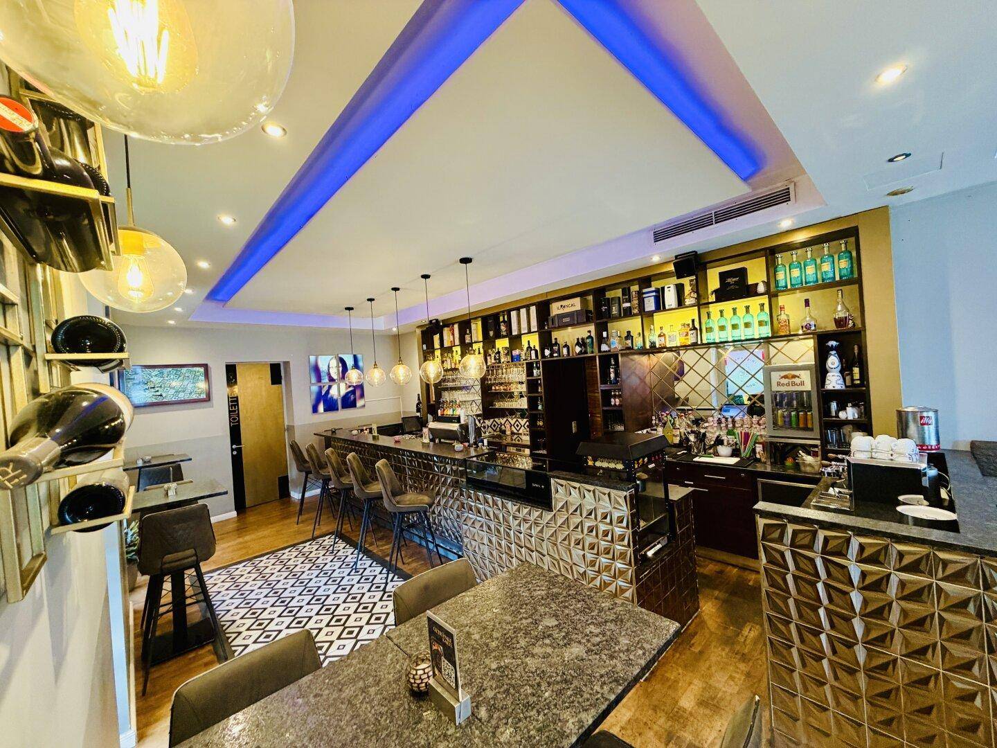 Elegante Bar mit beleuchteten Regalen, Flaschenauslage und dekorativer Deckenbeleuchtung.