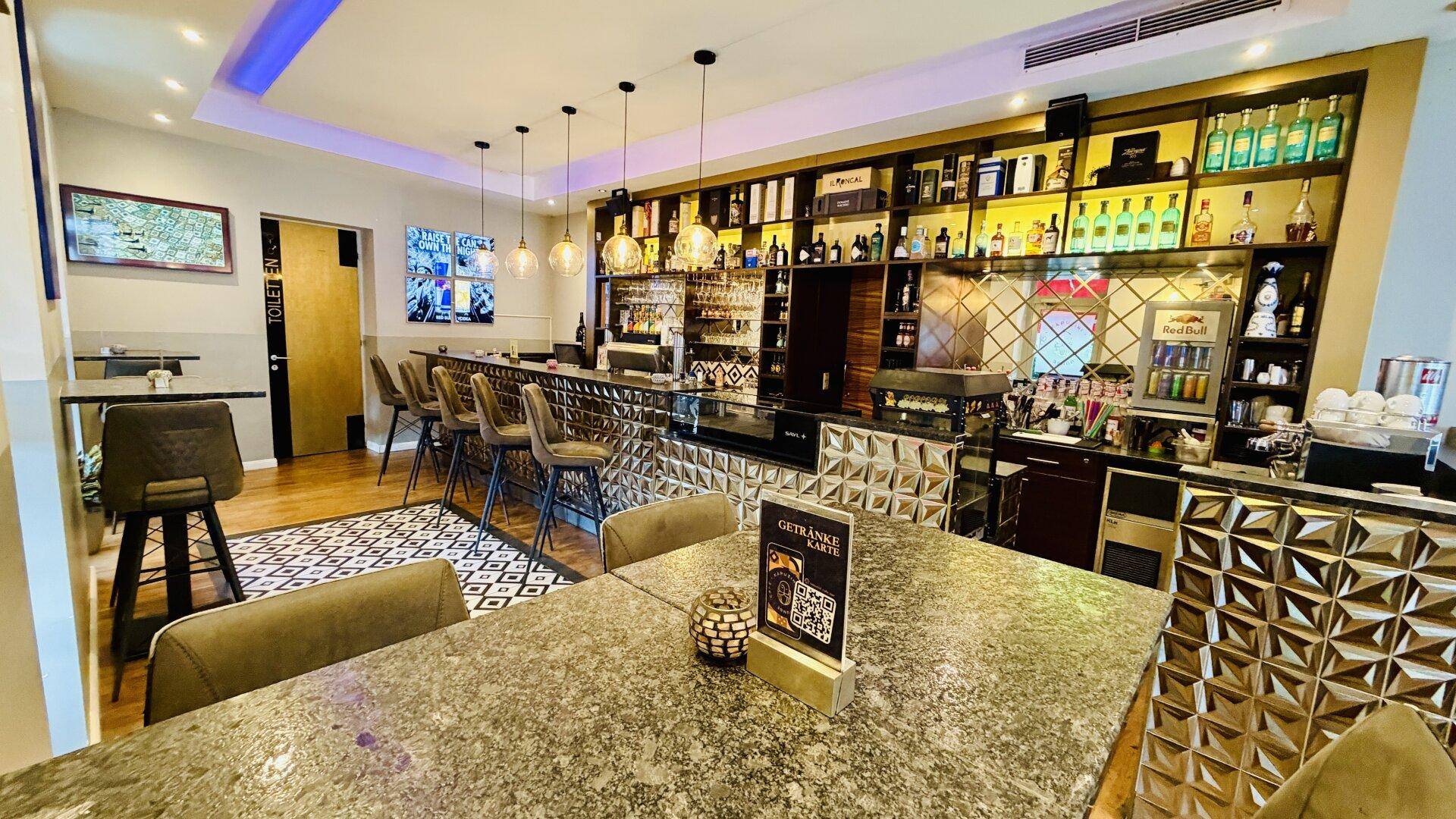 Moderne Bar mit umfangreicher Getränkeauswahl, stilvoller Beleuchtung und Sitzgelegenheiten im Vordergrund.