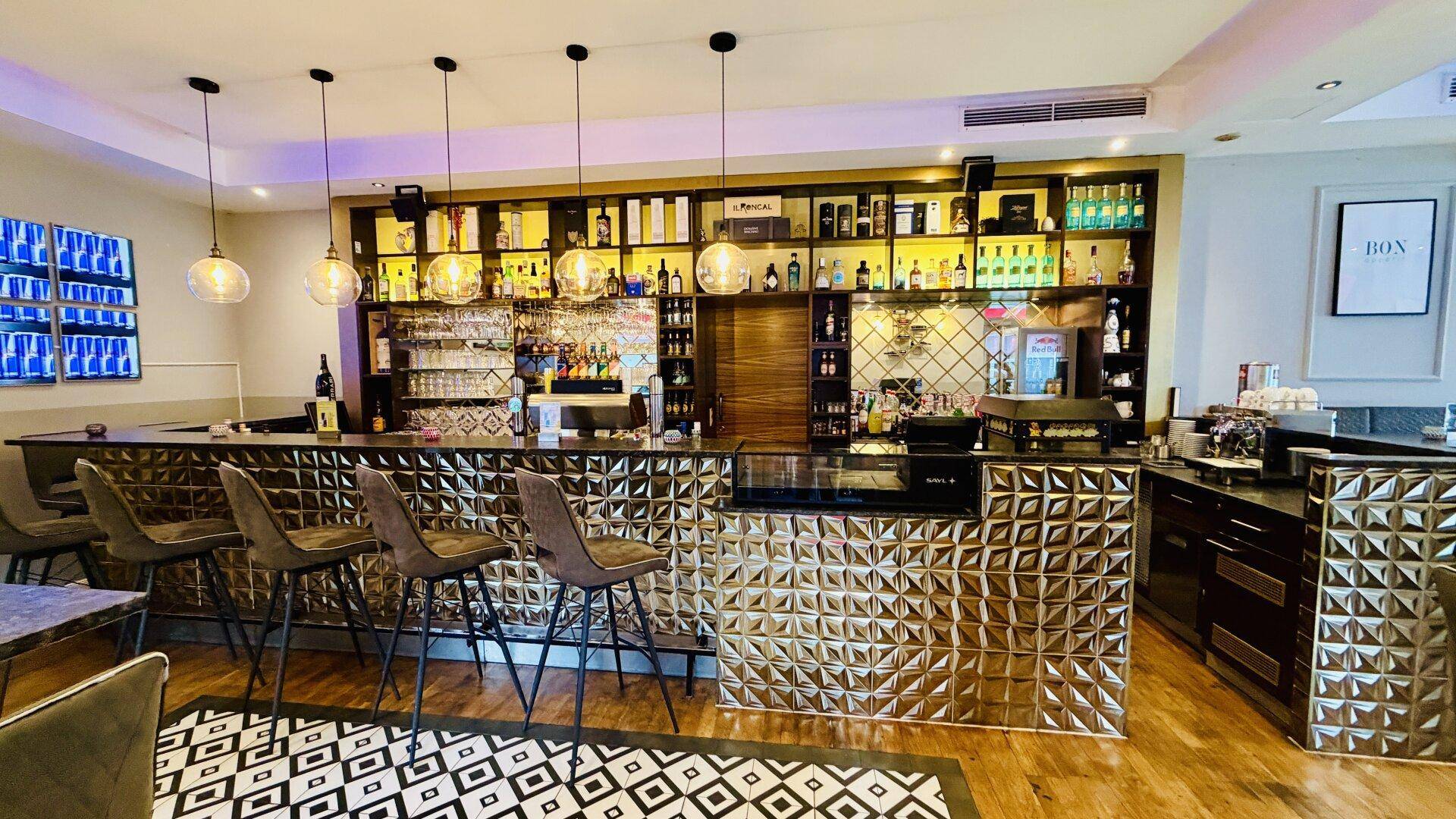 Gut ausgestattete Bar mit glänzenden Oberflächen, Barhockern und einer großen Auswahl an Getränken.
