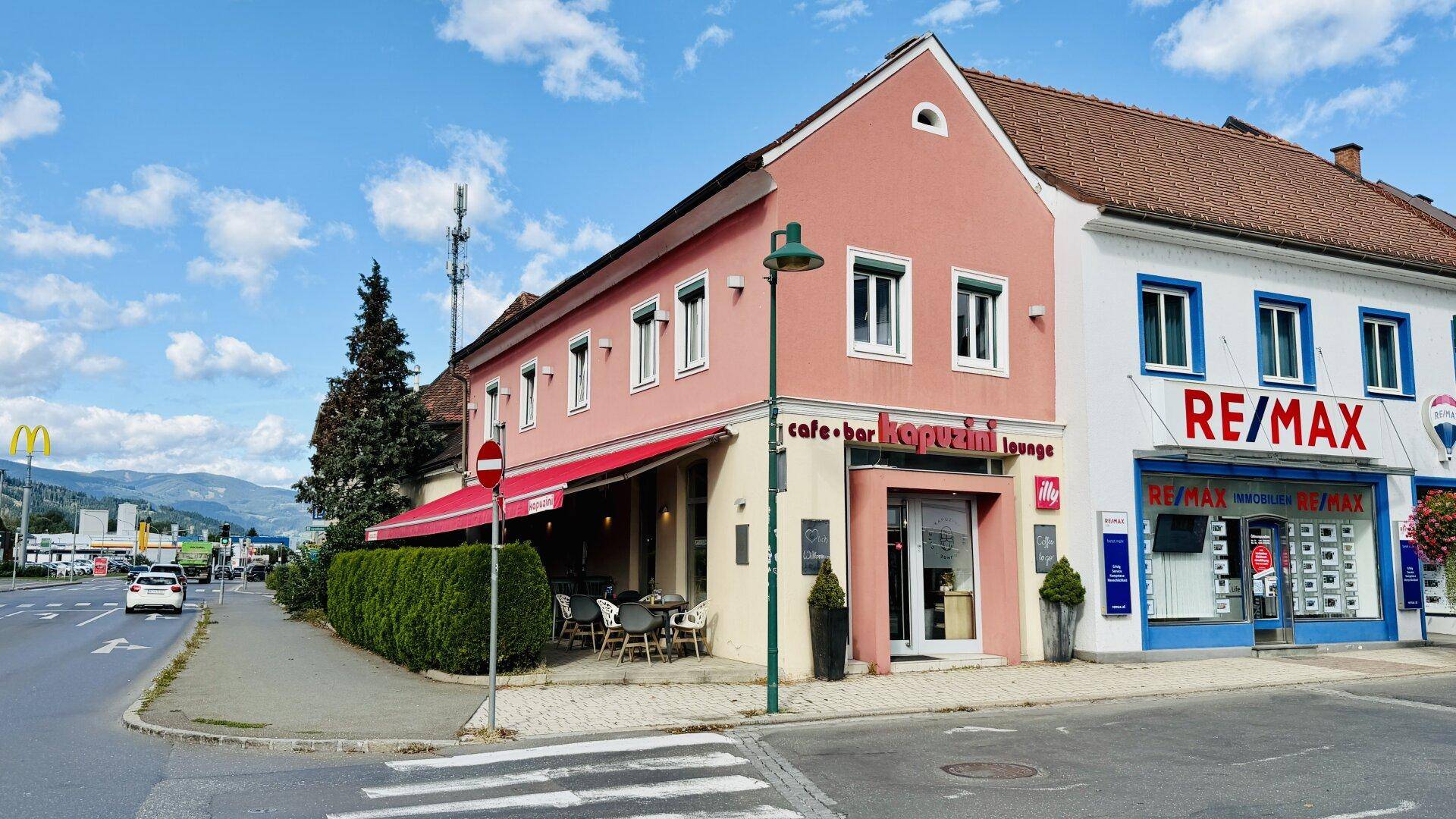 Außenansicht eines Gebäudes mit rosafarbener Fassade, Markise und angrenzendem Immobilienbüro.