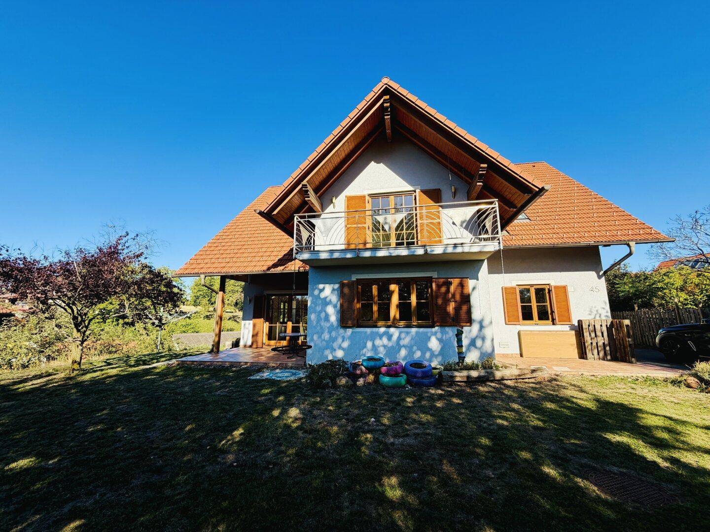 Hinteransicht des Hauses mit Garten, kleinem Balkon und überdachtem Terrassenbereich.